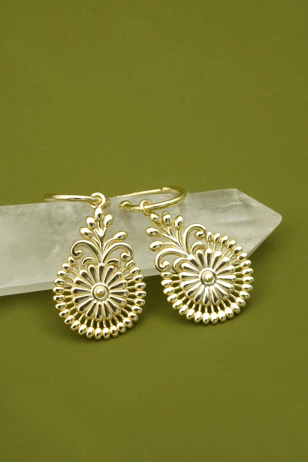 Gold paisley filigree flower earrings with intricate designs on a green background