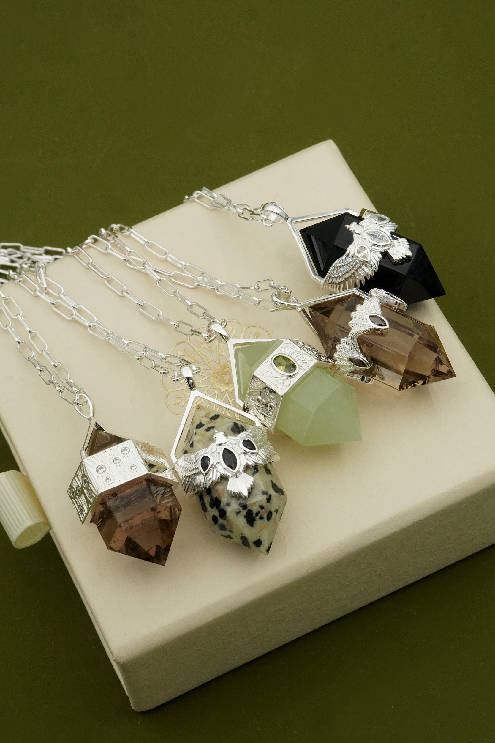 Set of gemstone nature-inspired pendants on silver chains displayed on a beige box with a green background