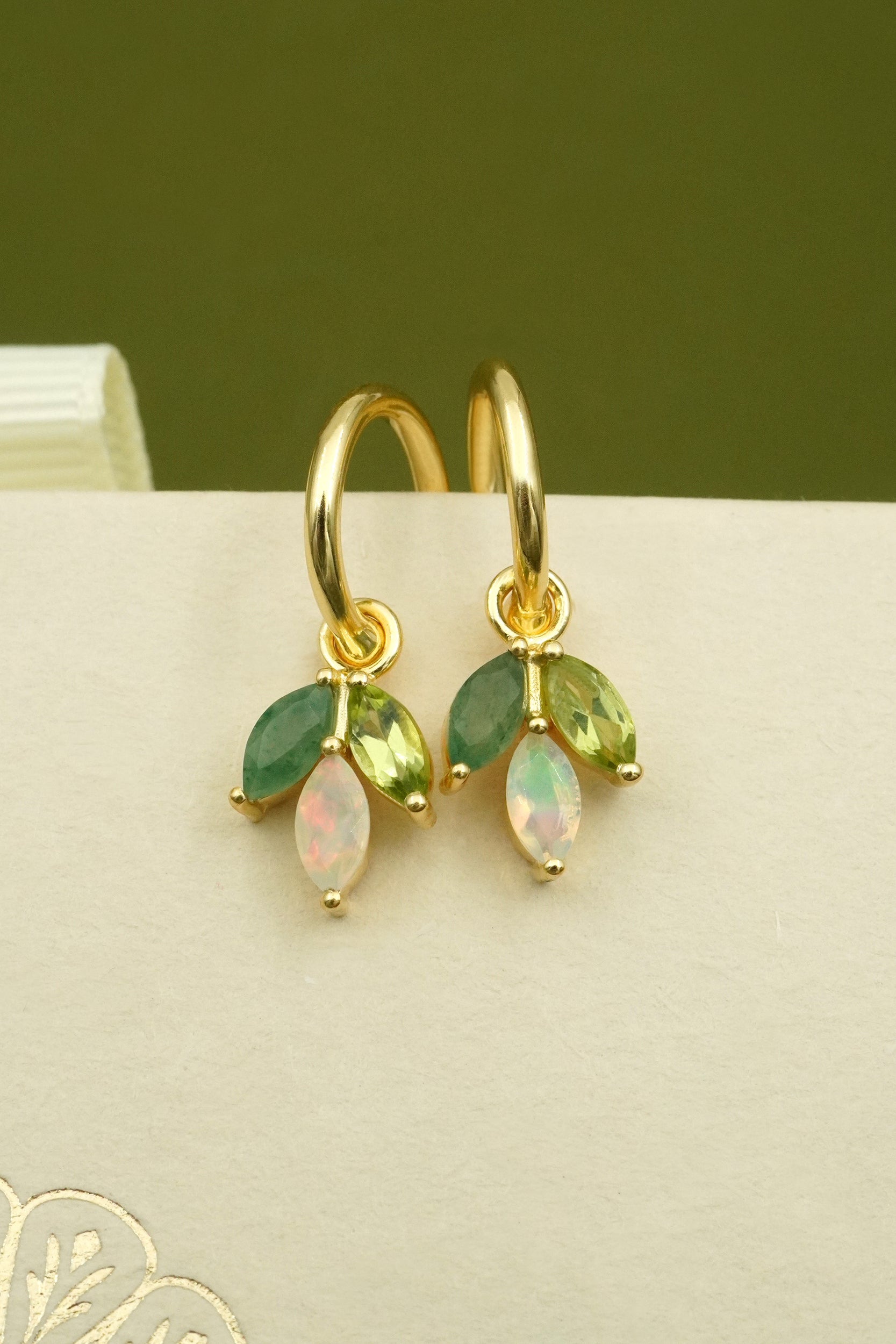 Gold earrings with green and opal stones on a green and beige background