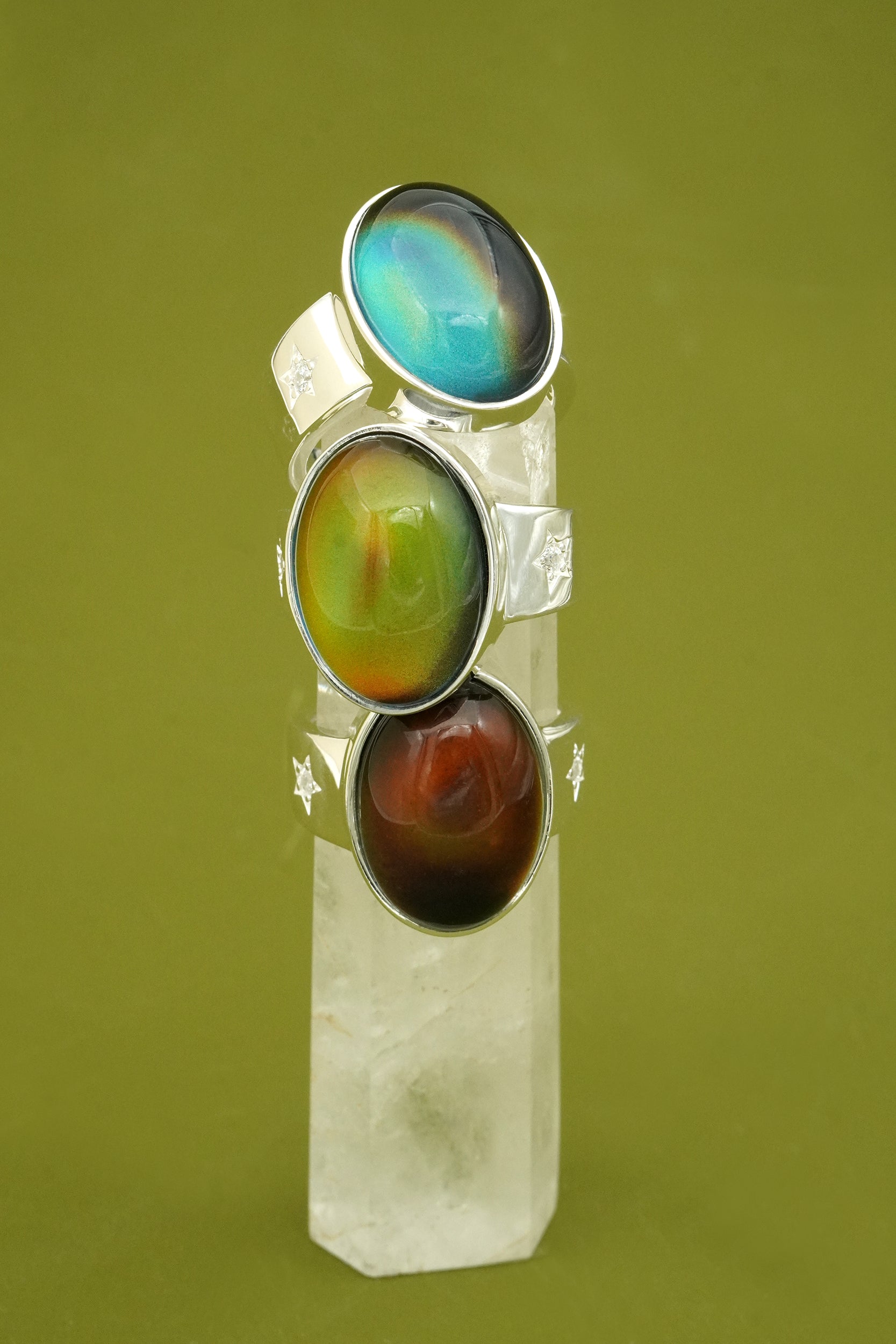 three Mood Rings on a clear stand against a green background
