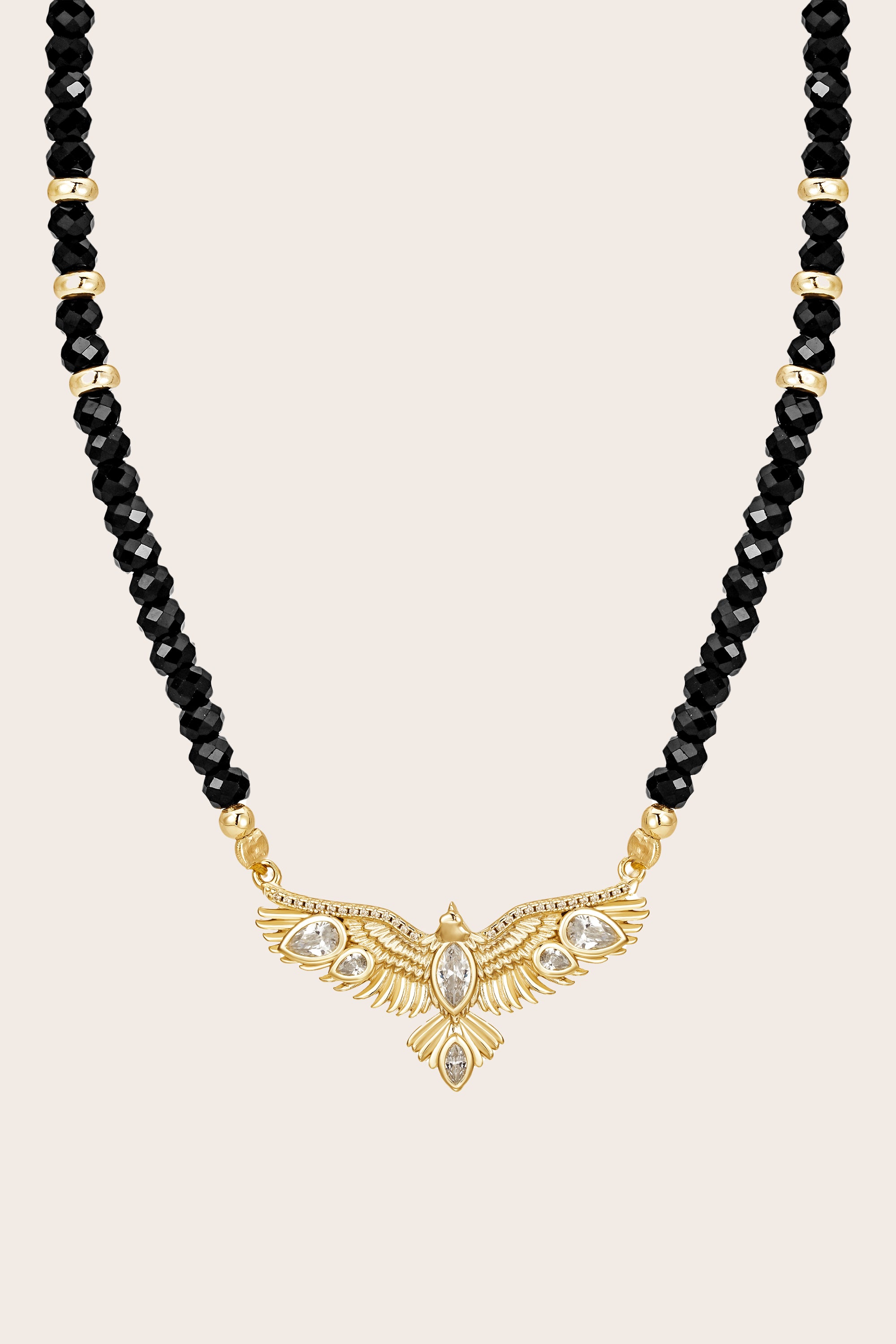 Necklace with black beads and a gold hawk pendant on a beige background