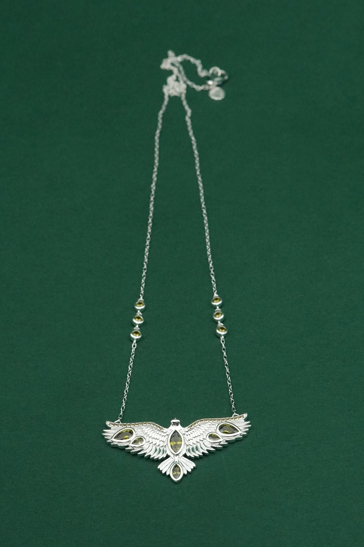 Silver necklace with an intricate wings open bird pendant on a green background