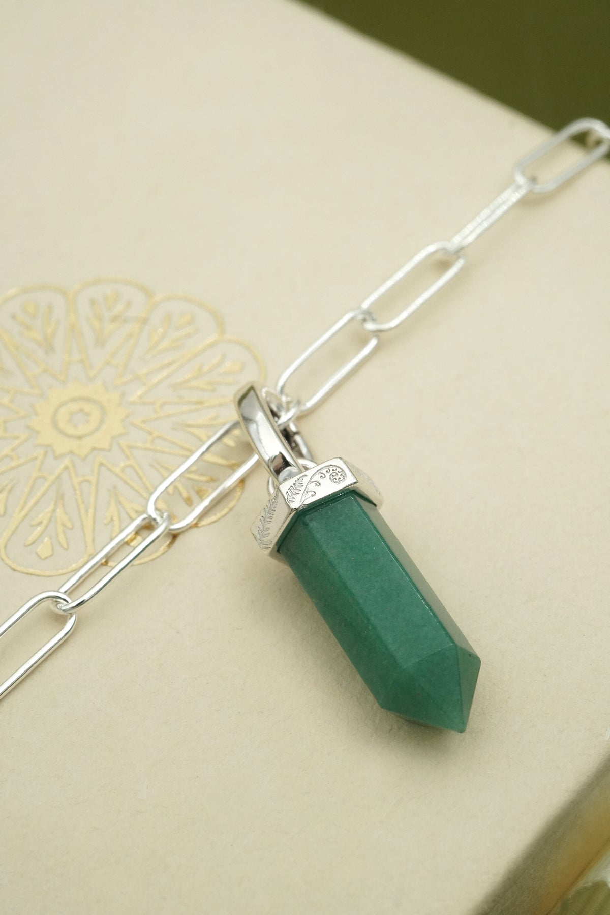Green aventurine crystal pendant on a silver chain against a beige background