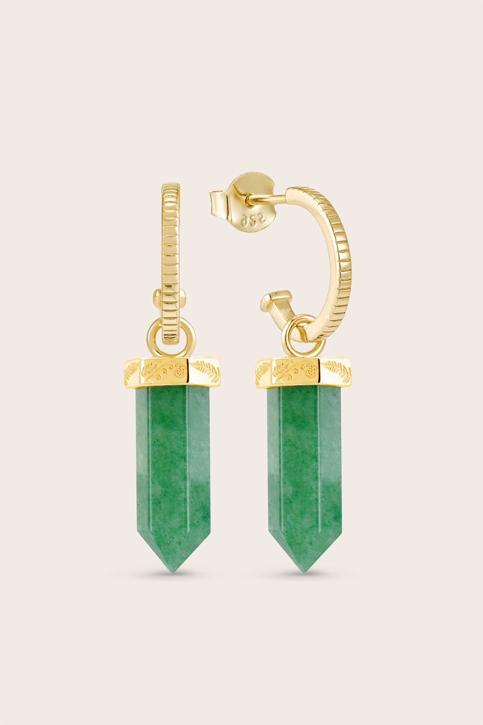 Gold earrings with green gemstones on a beige background