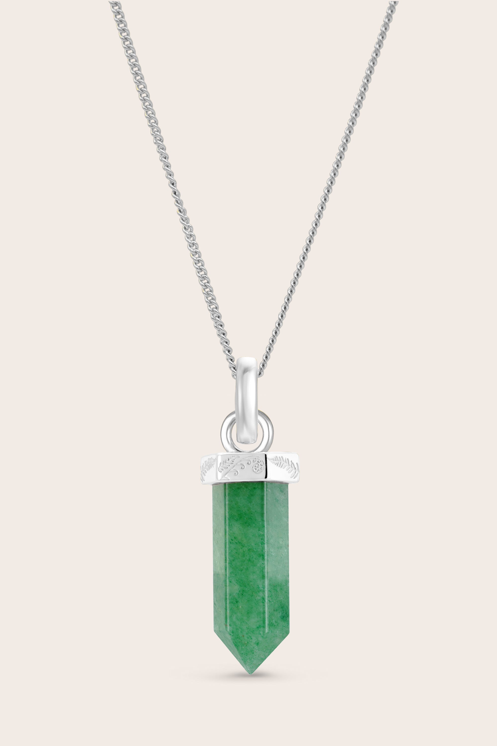 Green crystal pendant on a silver chain against a beige background