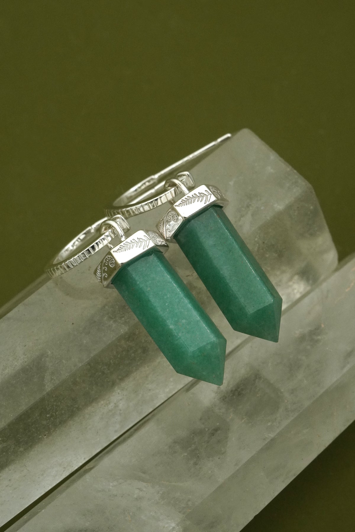 Silver earrings with green gemstones on a crystal surface