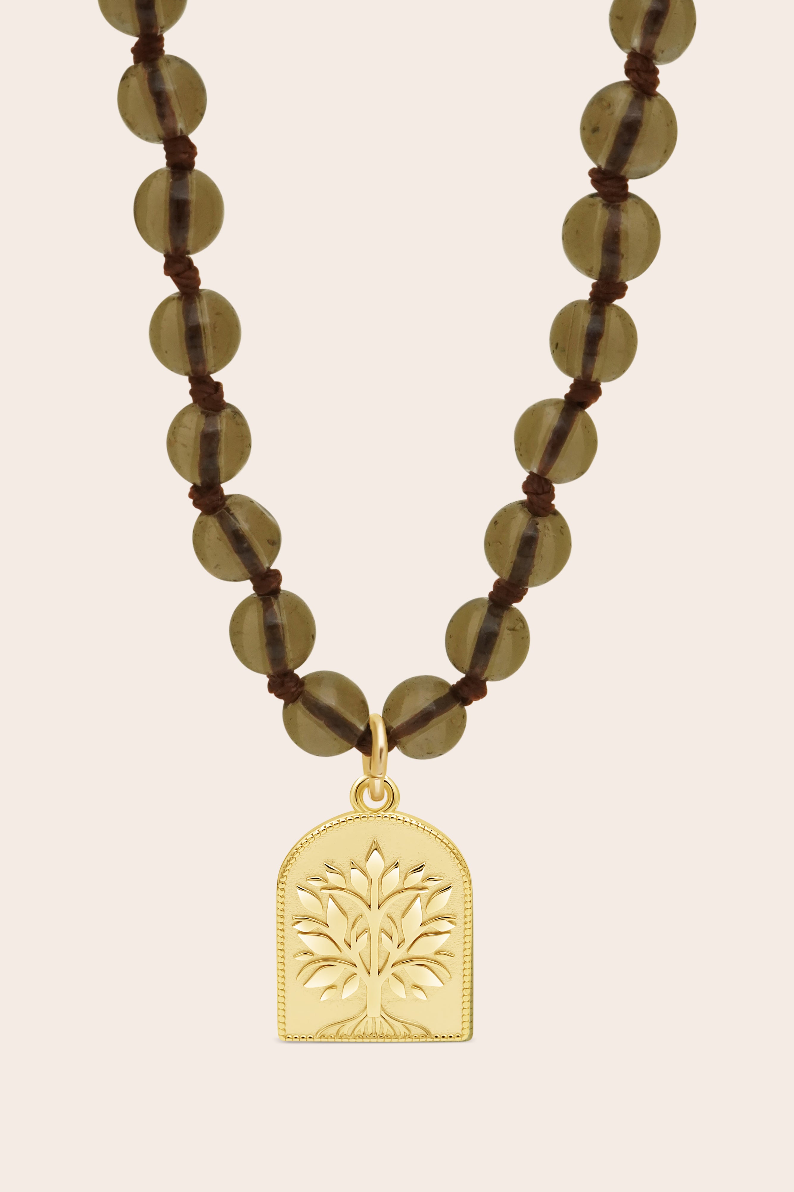 Necklace with smoky quartz beads and a gold tree of life pendant on a beige background
