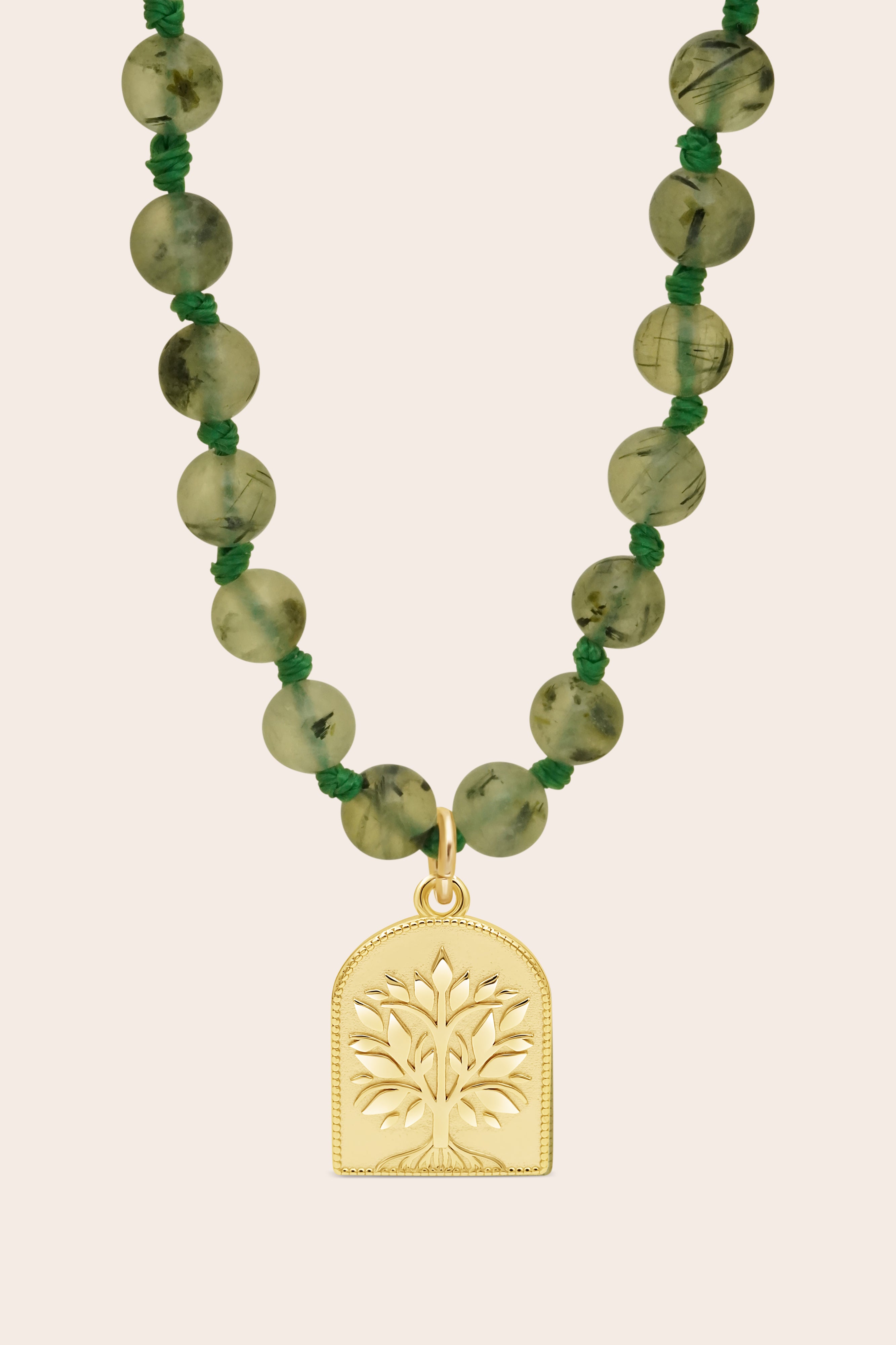 Necklace with green mala beads and a gold tree pendant on a beige background
