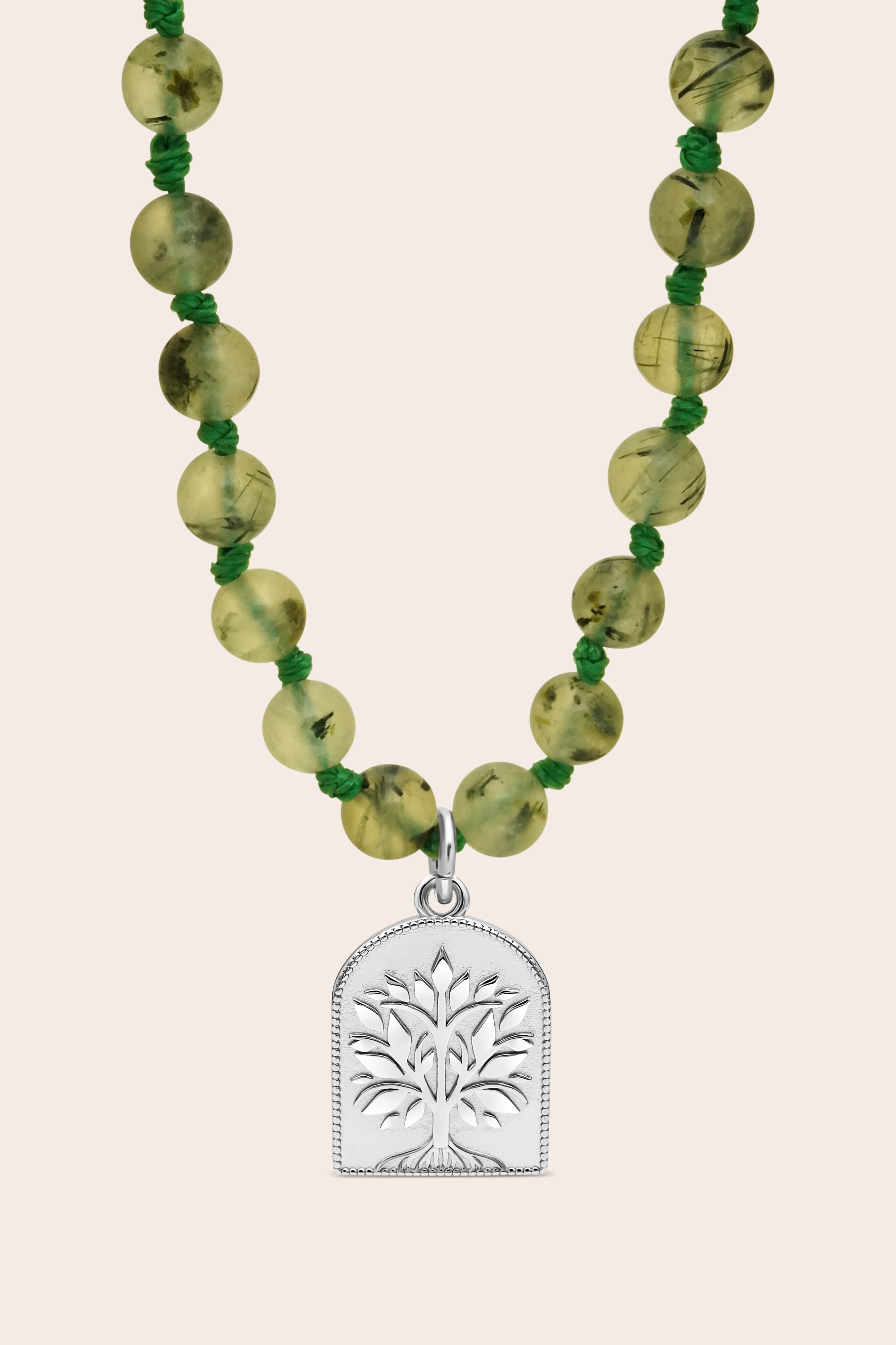 Mala Necklace with green beads and a silver tree pendant on a beige background