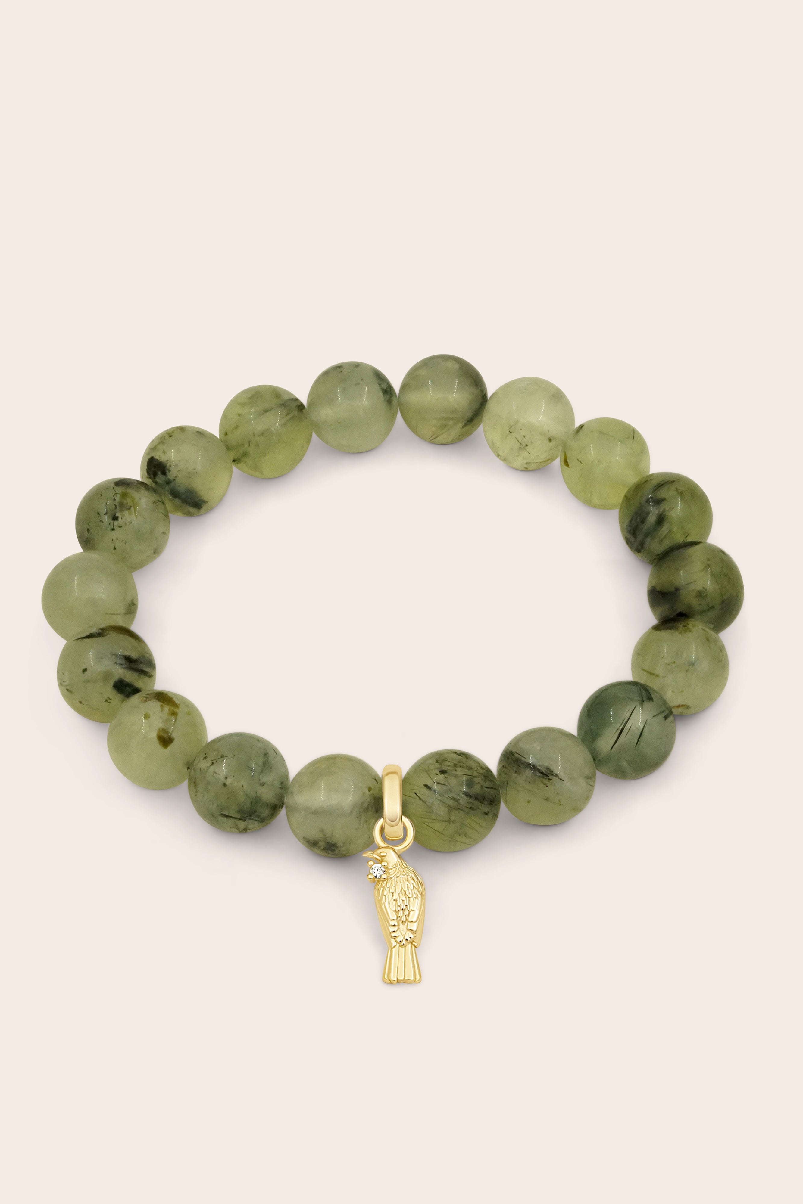 Green beaded gemstone bracelet with a gold Tui charm on a beige background