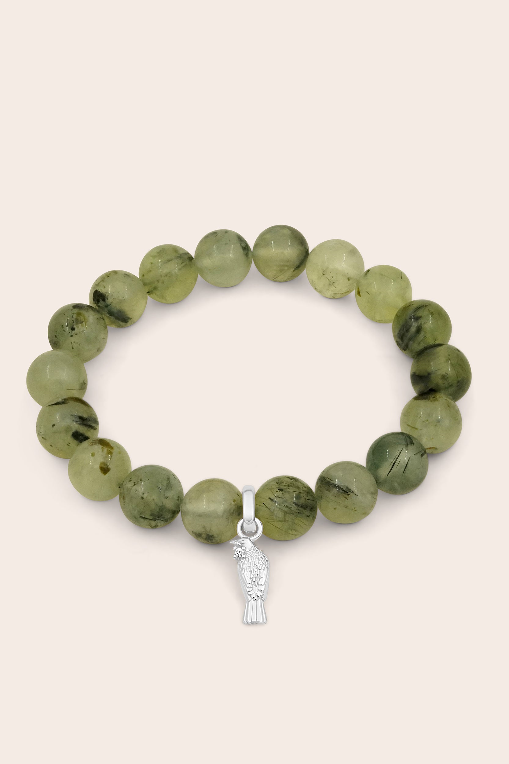Green beaded bracelet with a silver Tui bird charm on a beige background