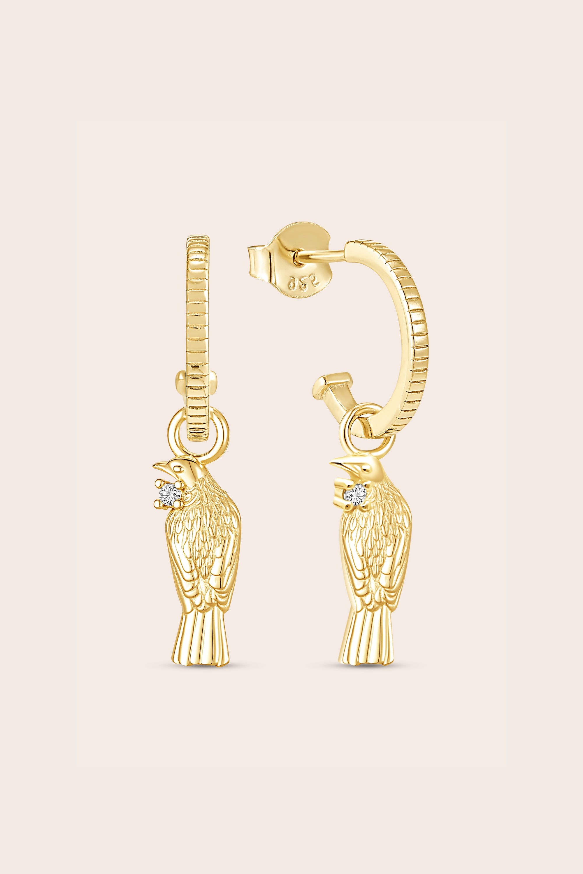 Gold tui bird-shaped earrings on a light beige background