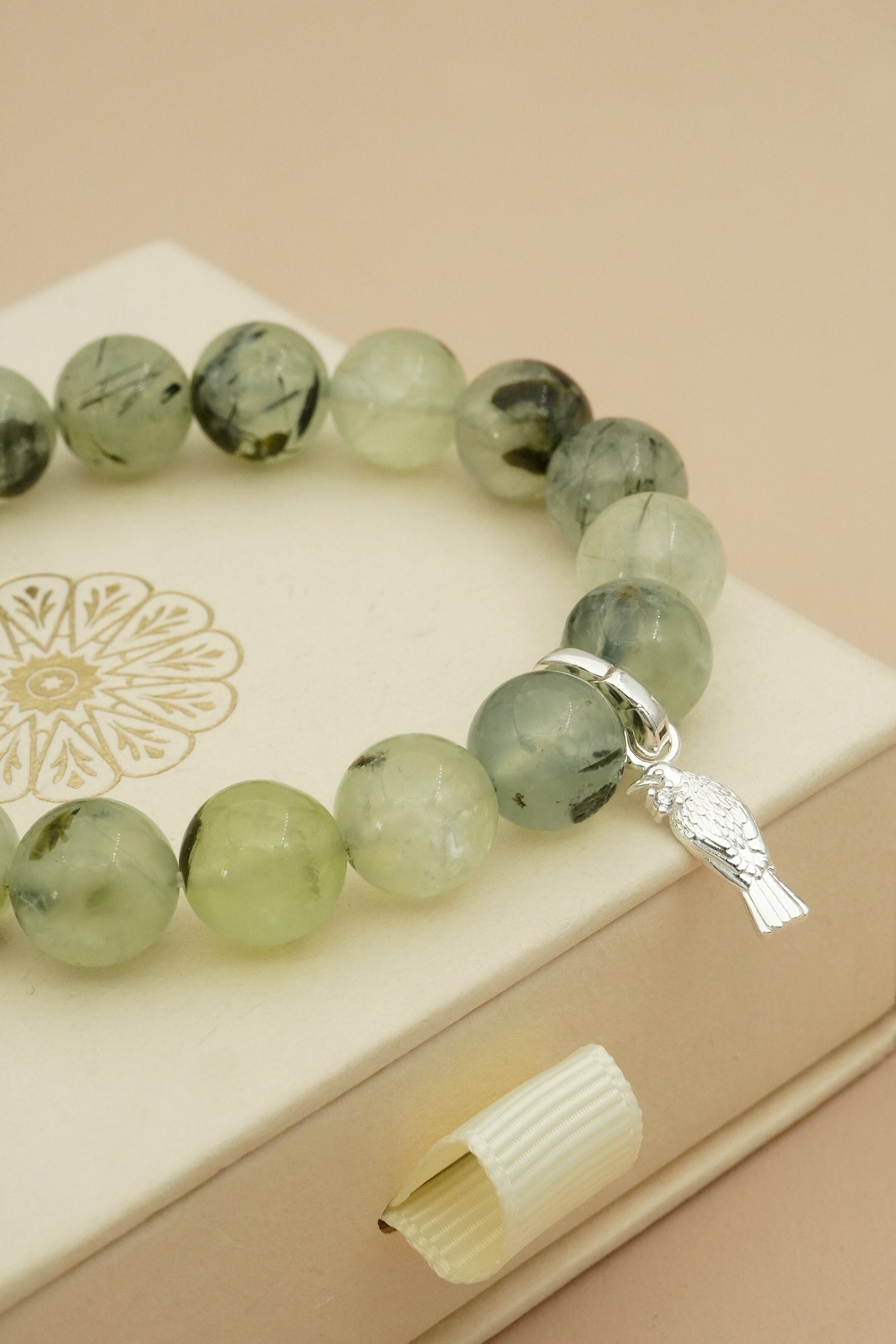 Green beaded bracelet with a silver Tui bird native to NZ charm on a beige surface