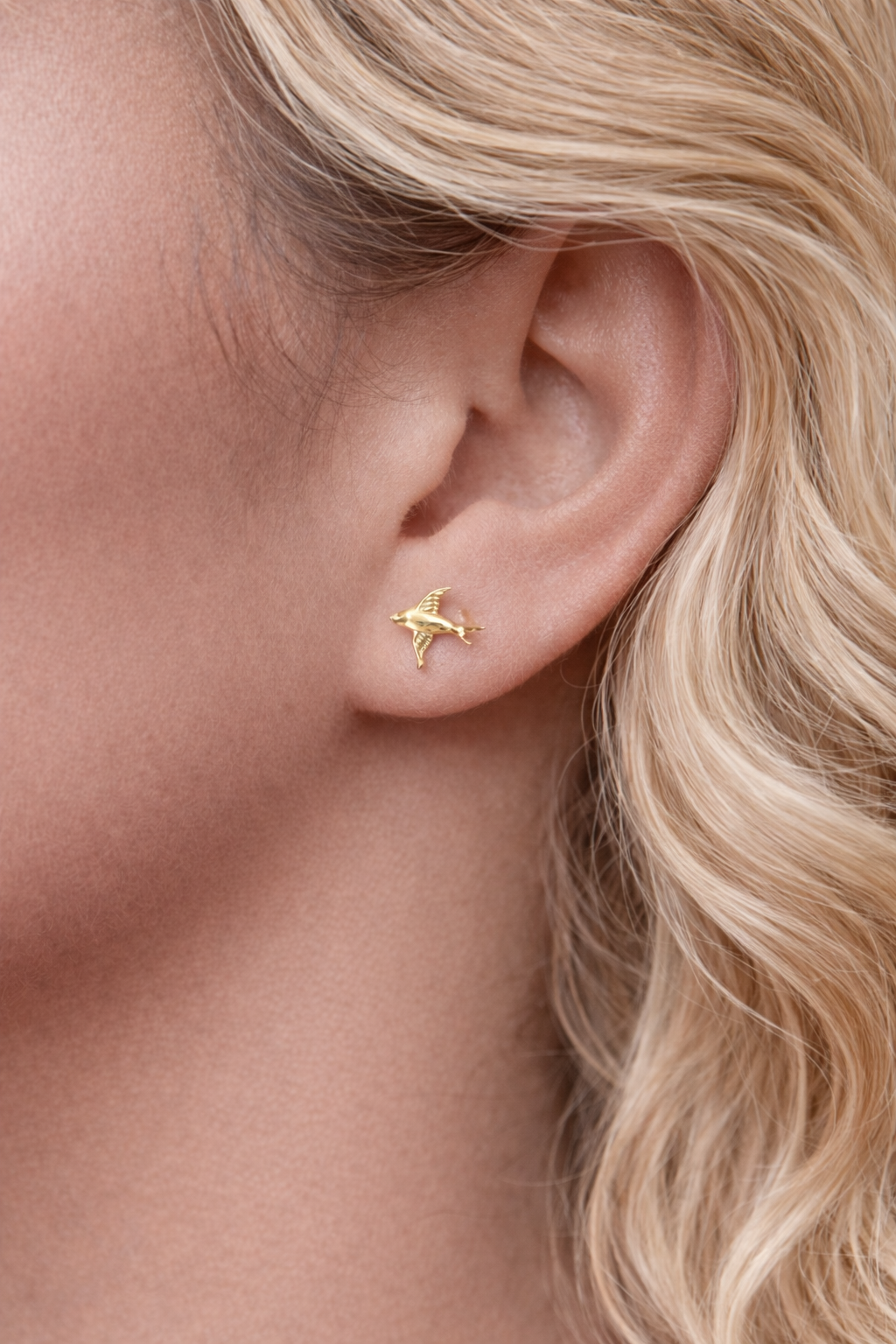 Gold bird earring worn by a person with blonde hair