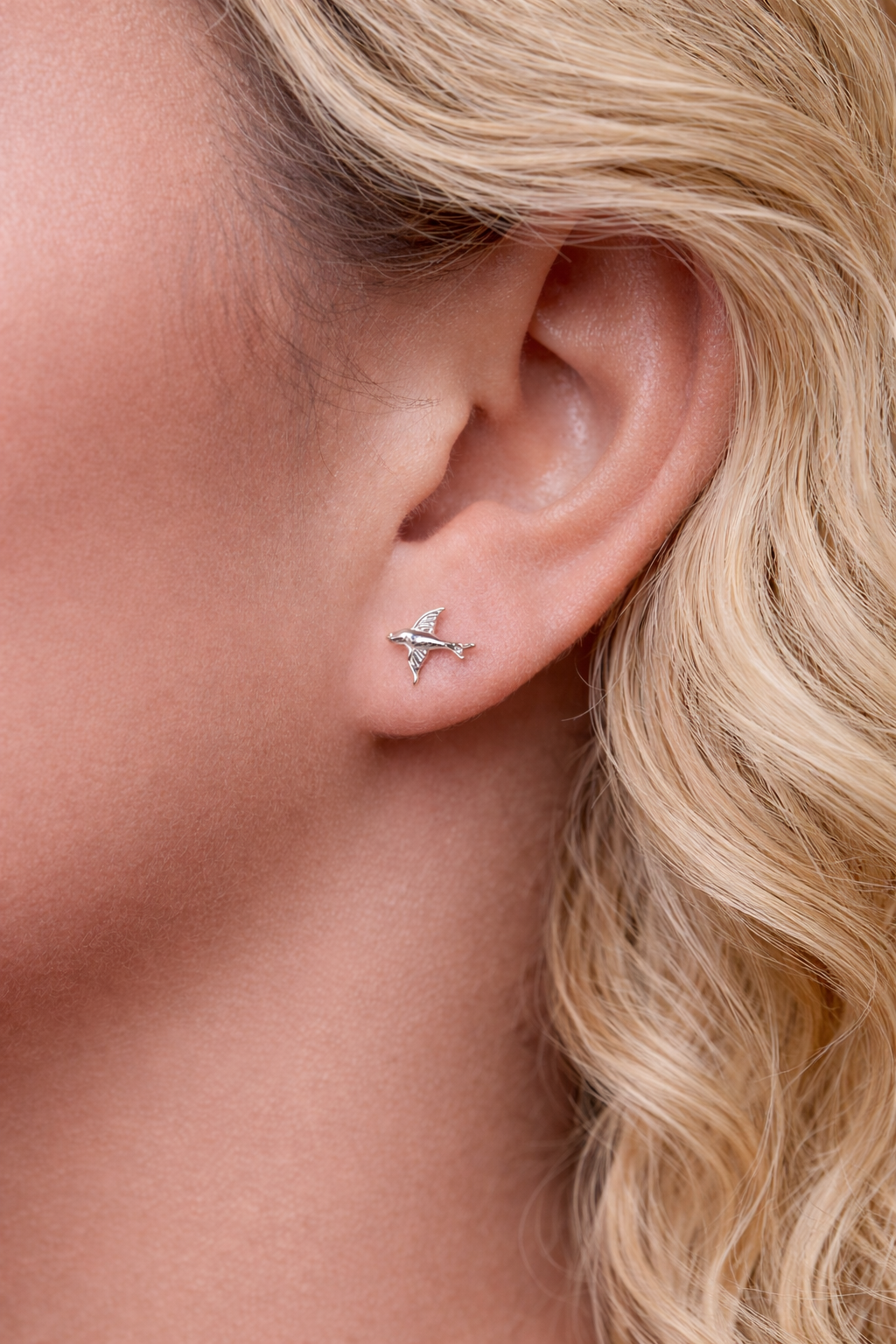 Close-up of a person wearing a bird stud with blonde hair.