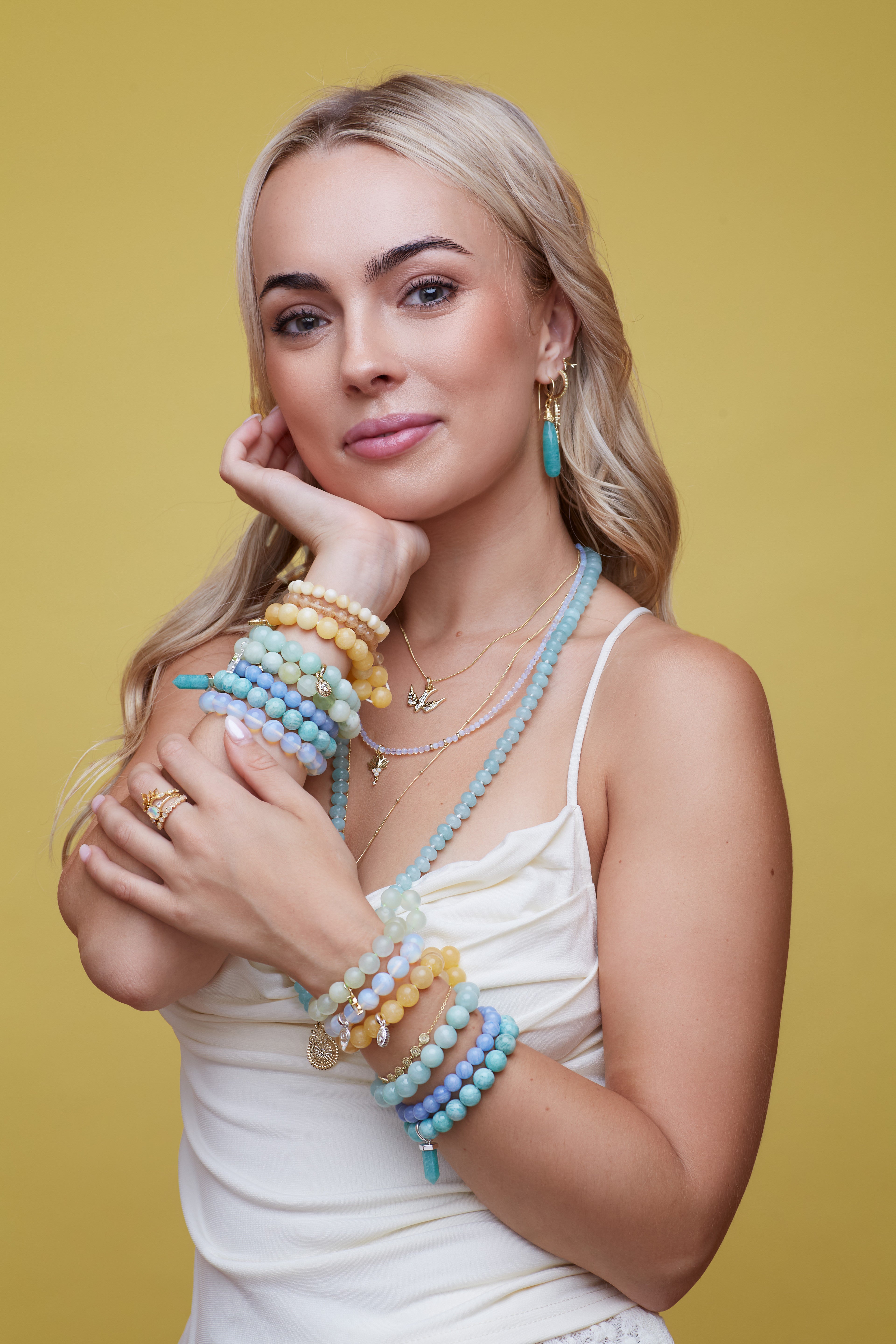 Woman wearing colourful beaded bracelets and necklaces on a yellow background
