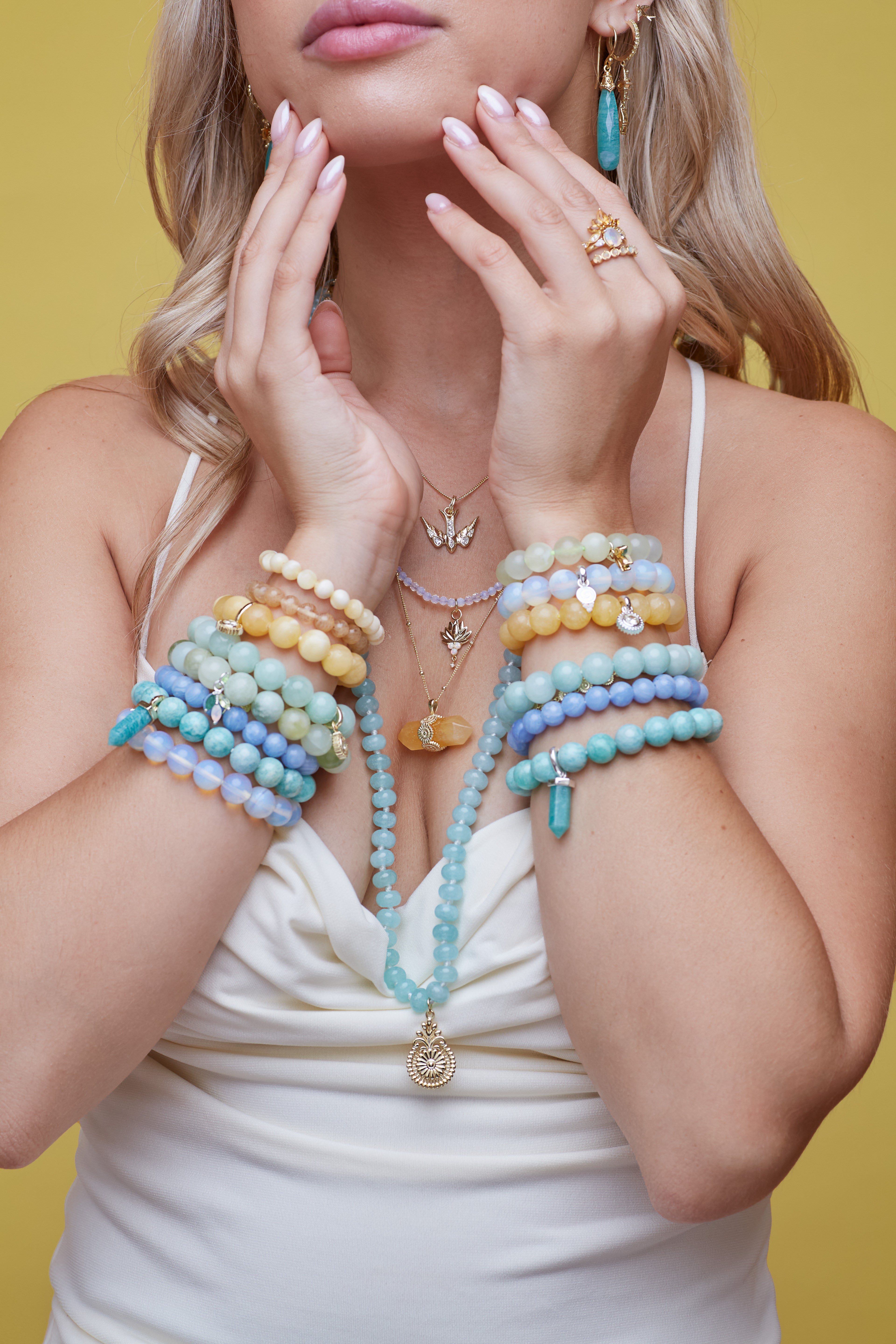 Woman wearing multiple colorful beaded necklaces and bracelets against a yellow background