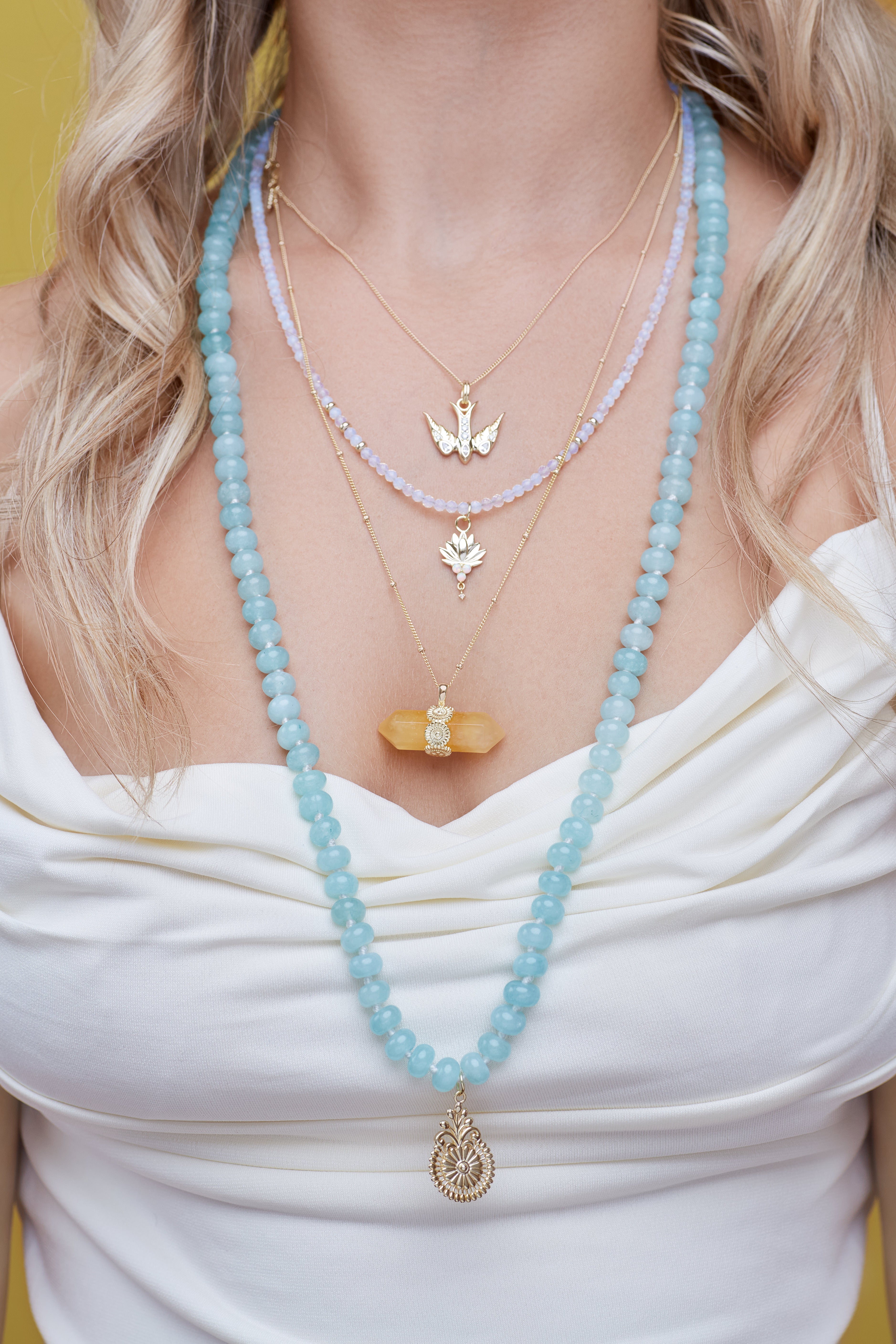 Close-up of a person wearing multiple necklaces with pendants on a blurred background