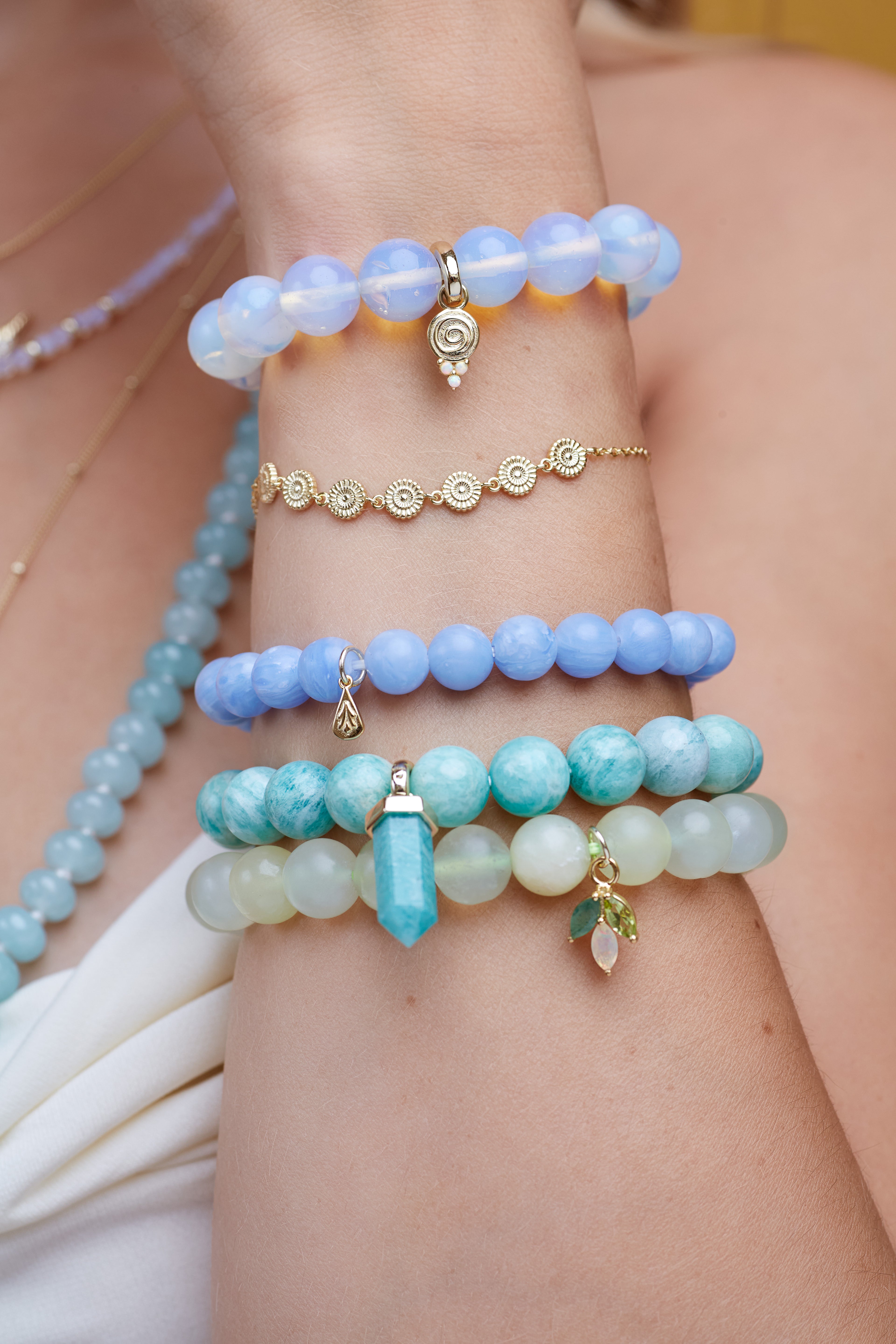 Close-up of a person's wrist wearing multiple gemstones bracelets with blue, green, and gold accents.