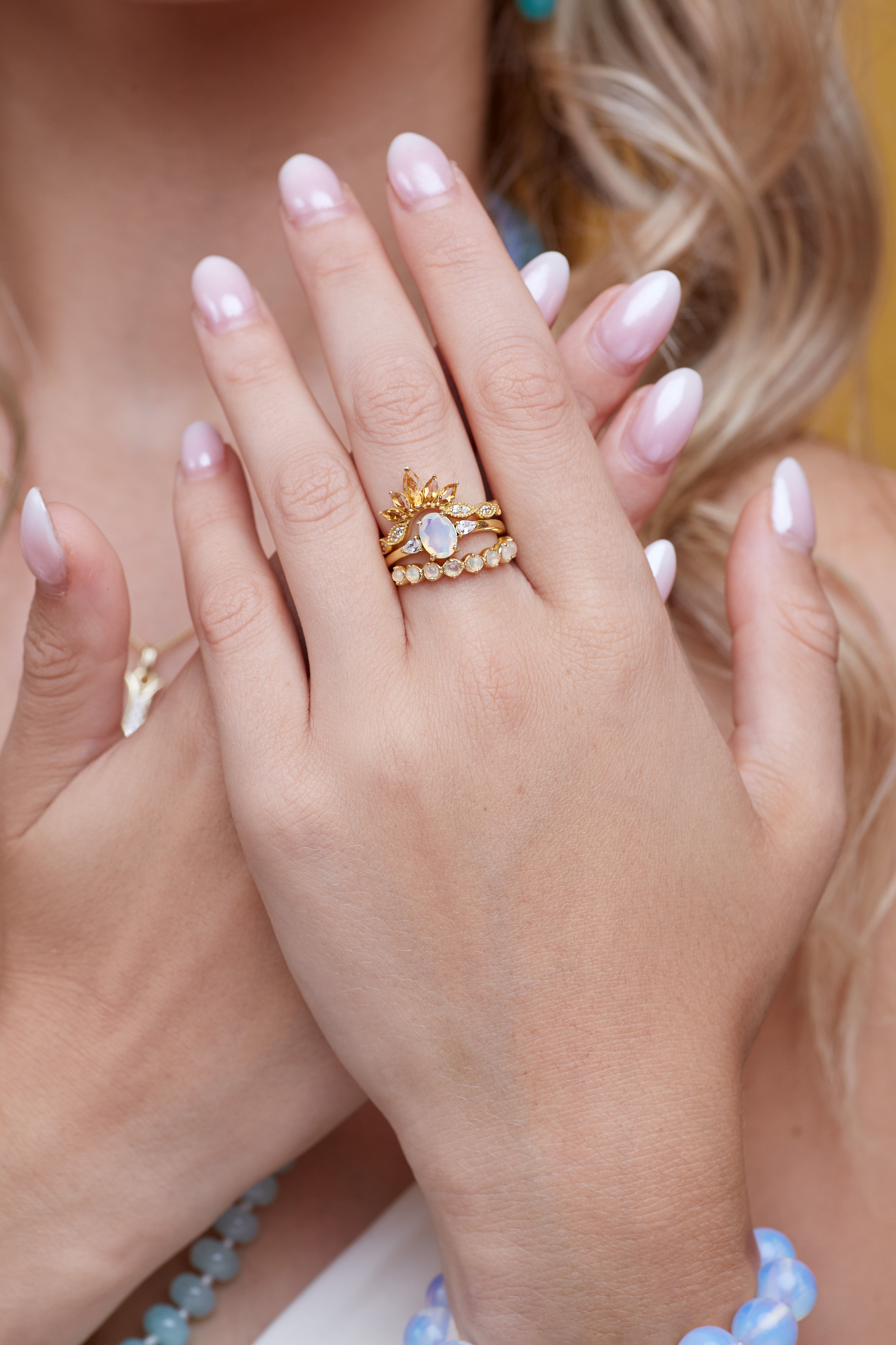 Close-up of hands with gold rings and pink nail polish against a blurred background
