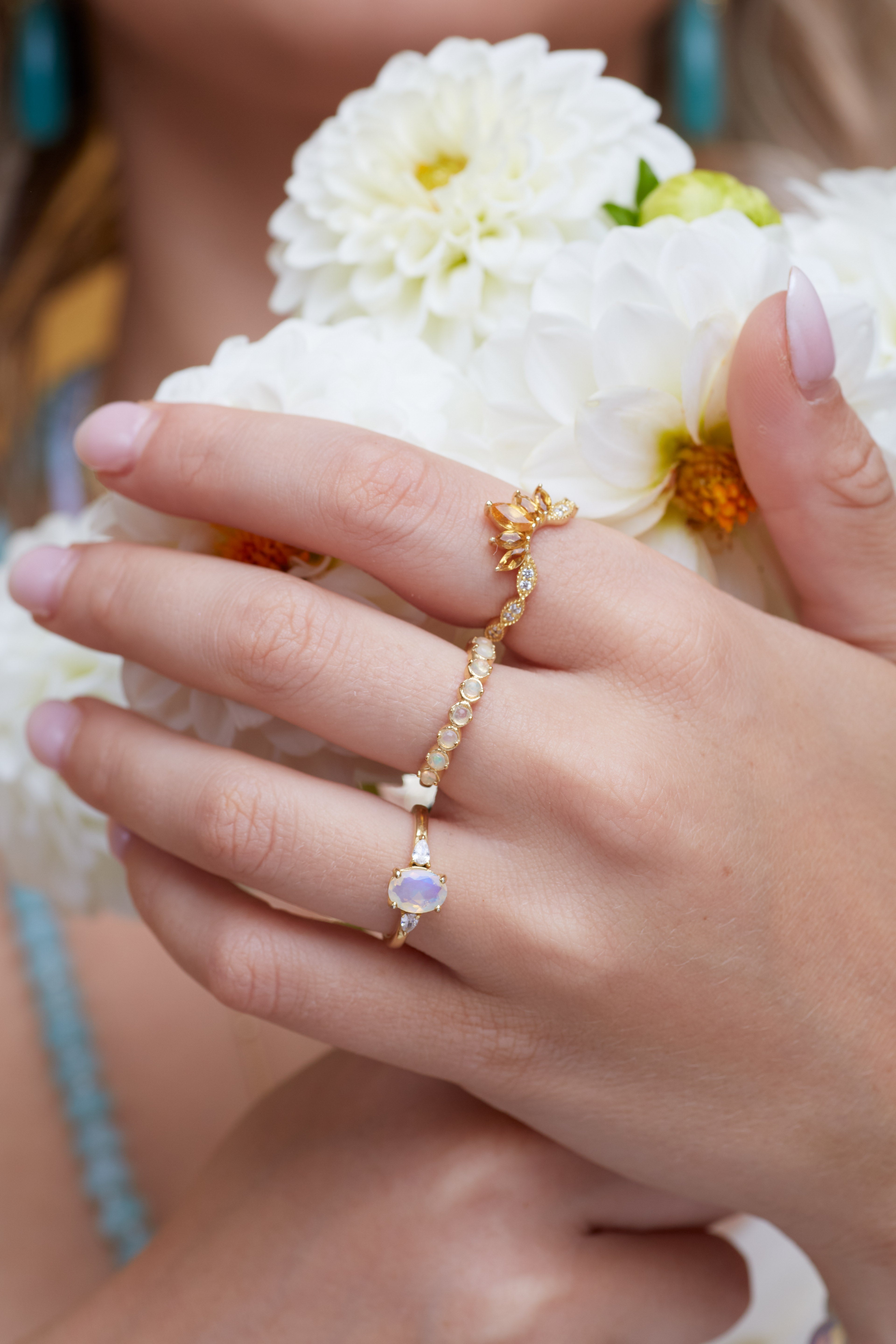 Hand wearing a gold rings with opal gemstones, holding white dahlias