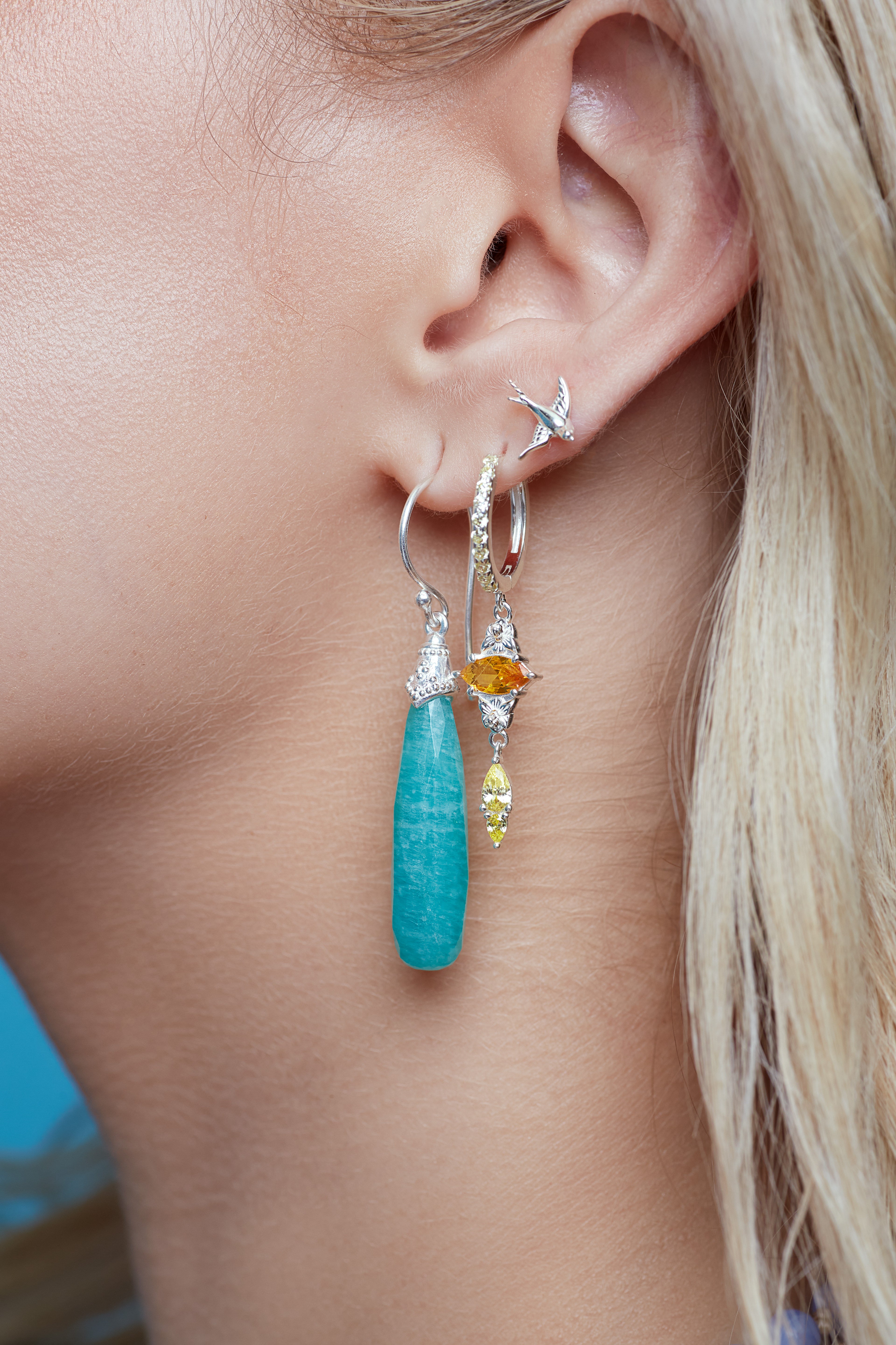 Close-up of a person wearing a turquoise amazonite earring with a yellow gemstone.
