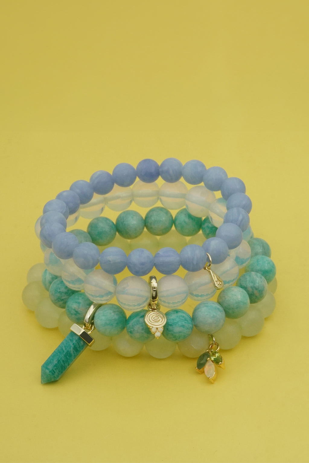 Stack of beaded gemstone bracelets with charms on a yellow background