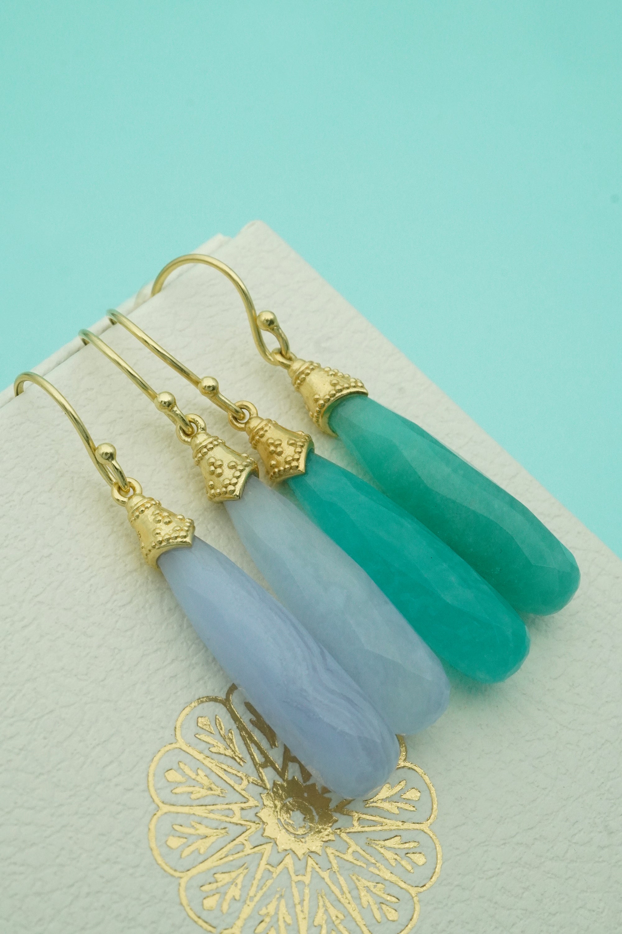 Pair of earrings with green and white stones on a decorative card with a gold design.