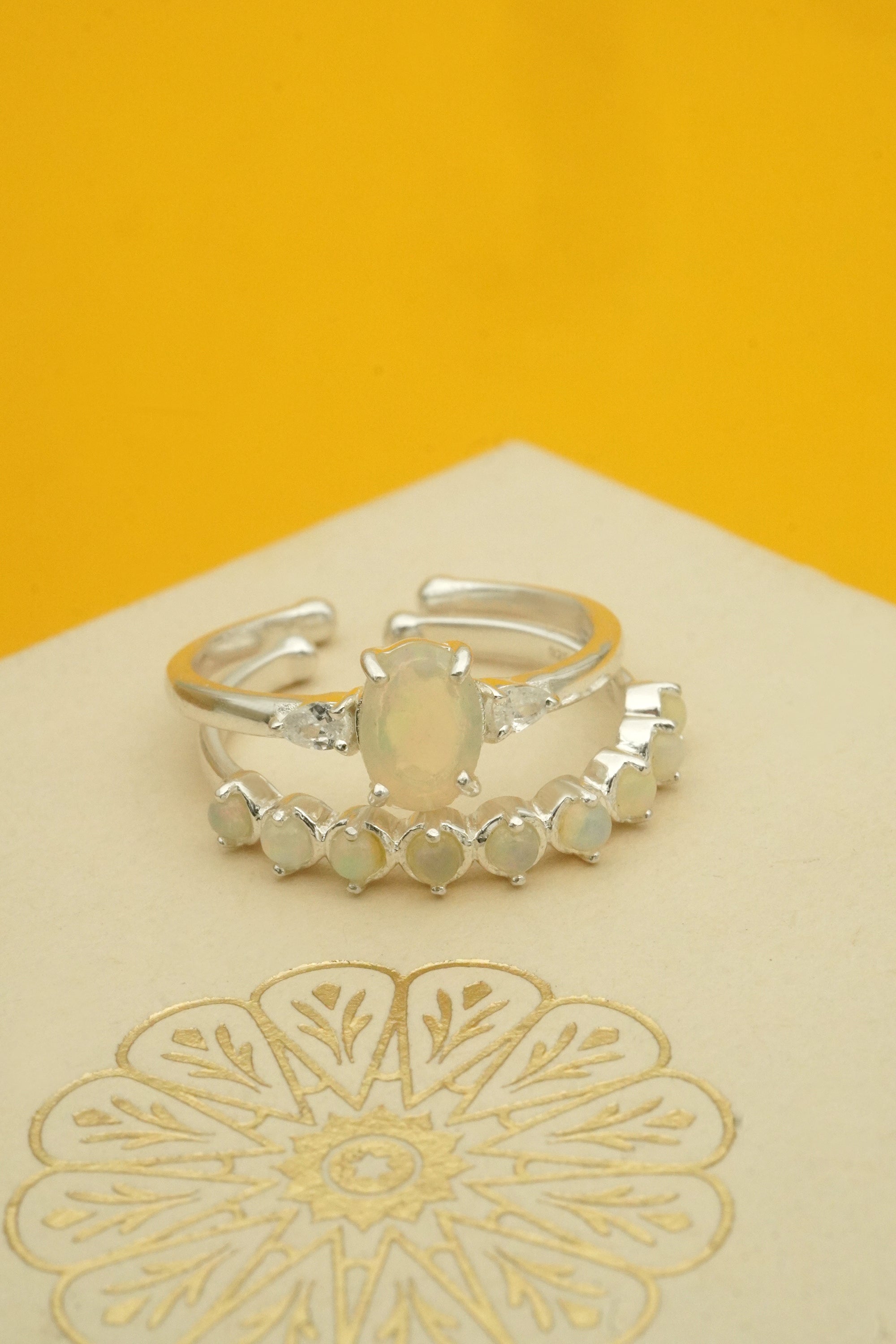 Silver stacking rings with a central opal stone on a yellow background
