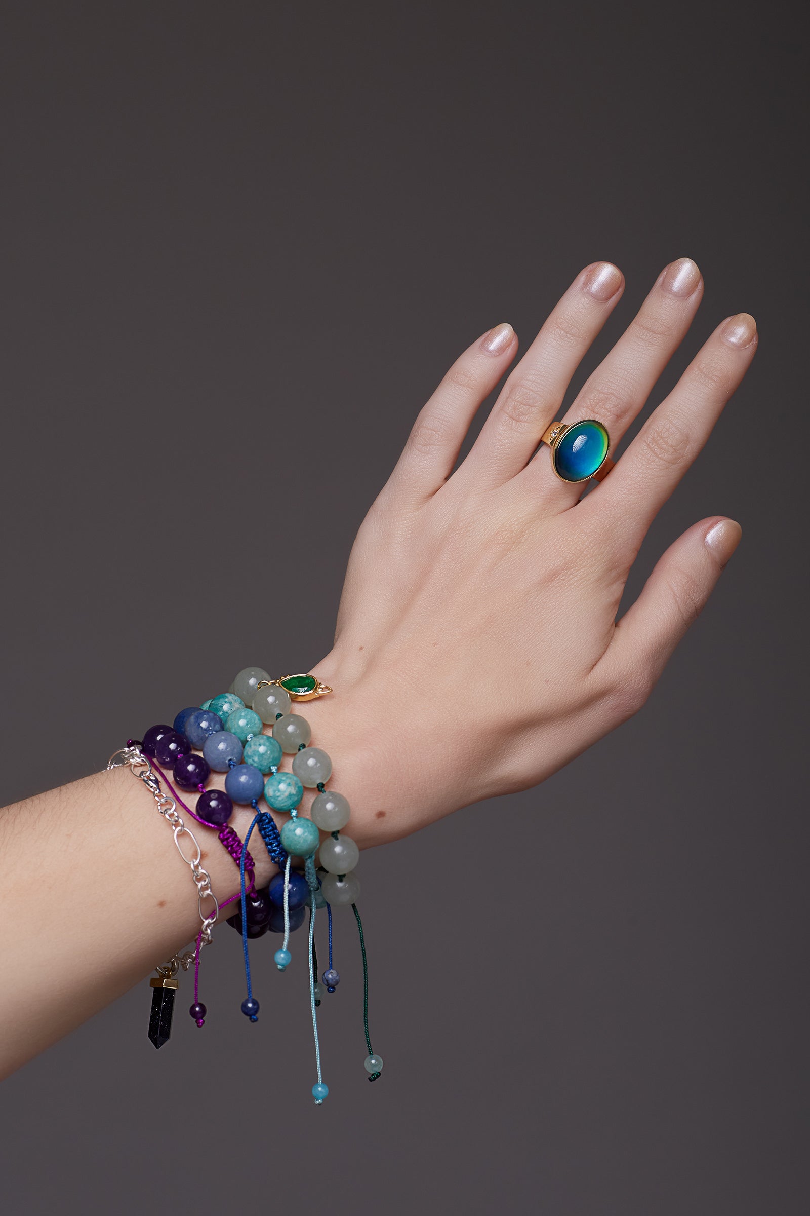 Hand wearing colourful mood ring on a dark background