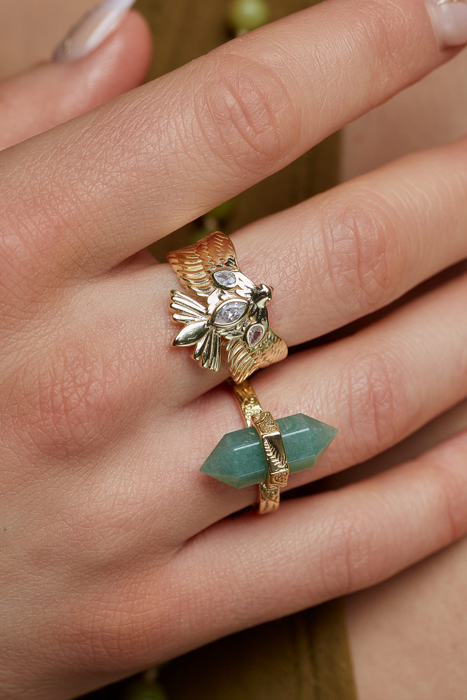 Close-up of a hand wearing two gold rings with gemstones on a neutral background