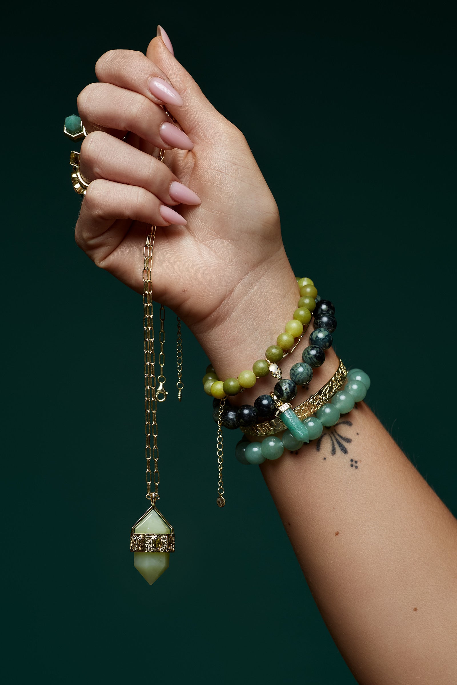 Hand wearing multiple spiritual gemstone bracelets with green crystal beads against a dark background