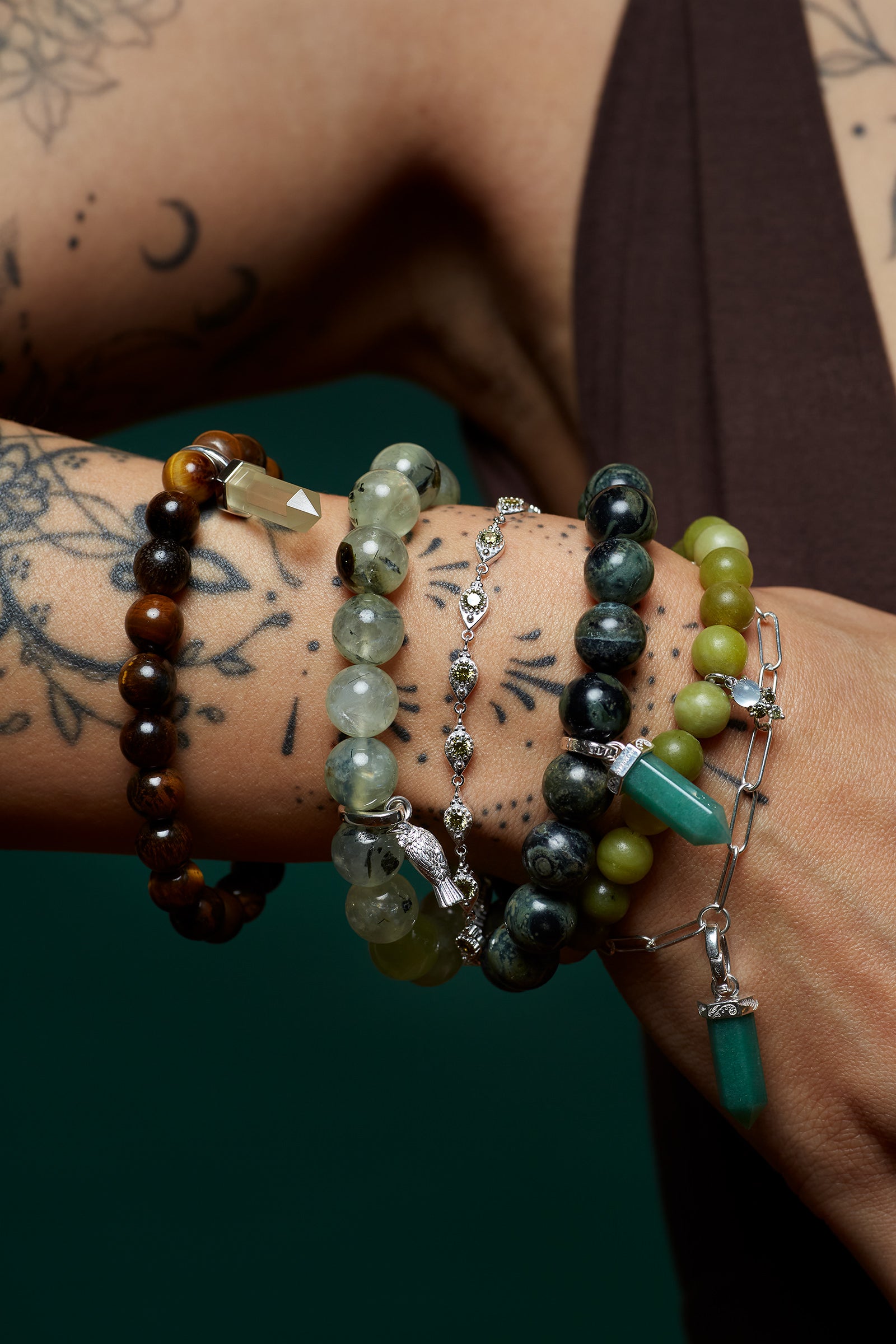 Close-up of a wrist wearing multiple green and brown spiritual beaded bracelets with a tattooed arm.