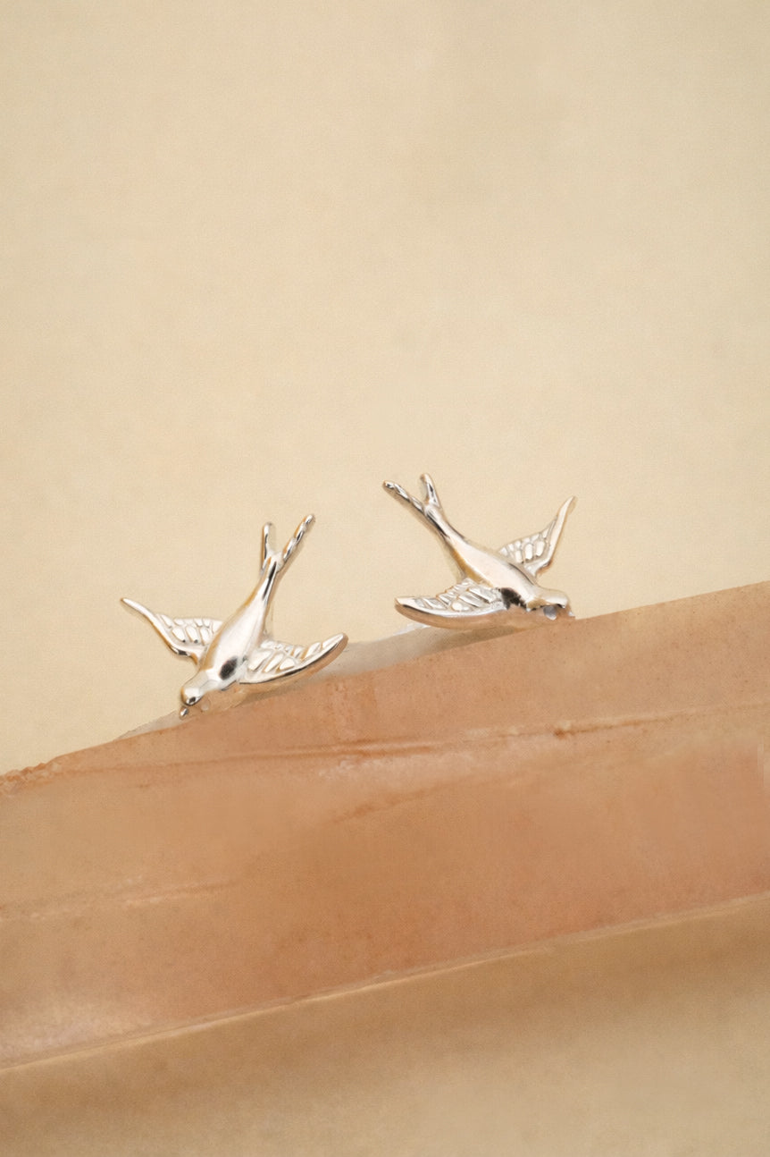 Silver bird-shaped earrings on a beige background