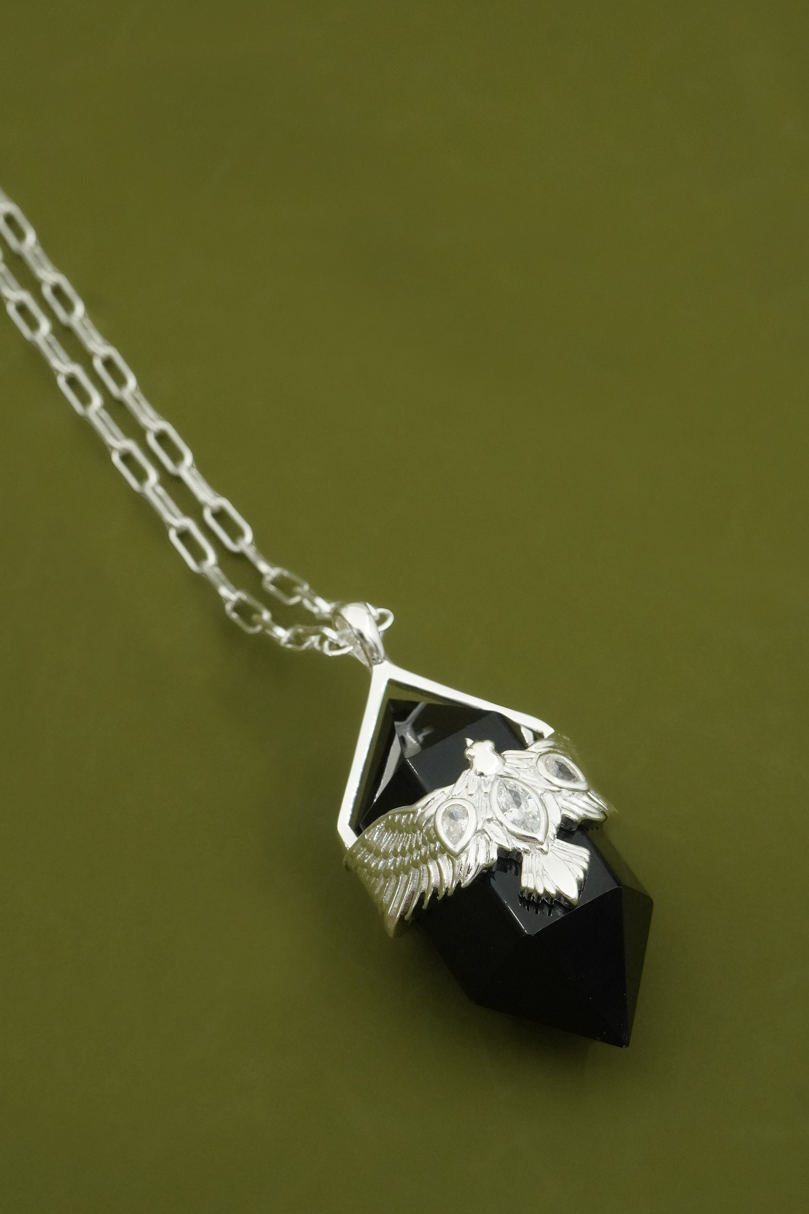 Black agate crystal pendulum necklace with sterling silver bird wing design on a green background