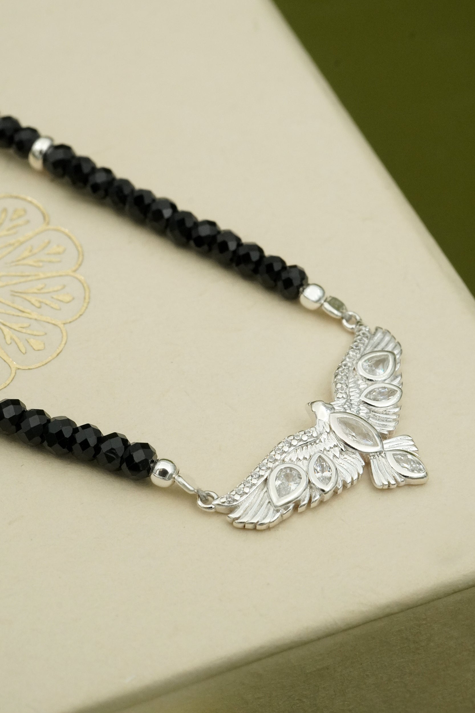 Necklace with black beads and silver hawk pendant on a beige surface
