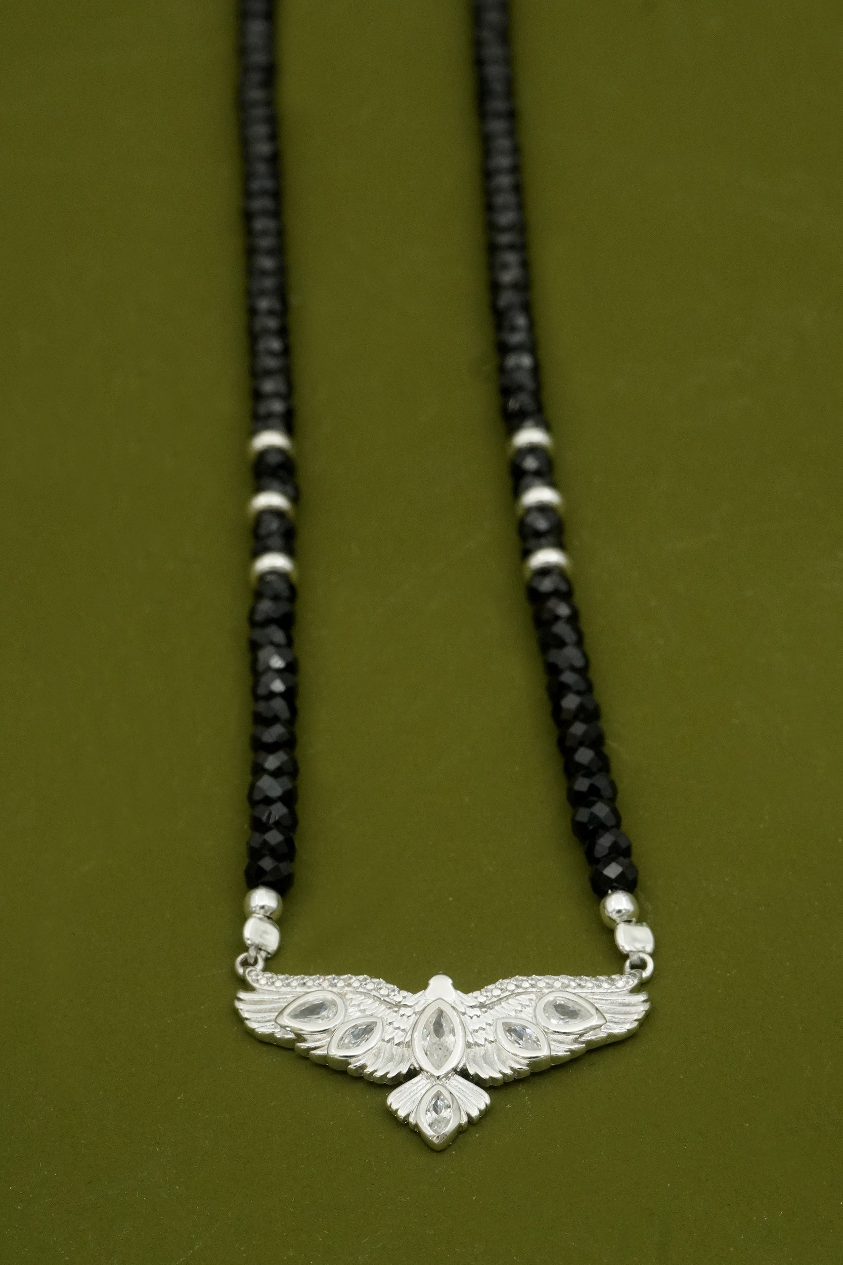 Necklace with black beads and a silver hawk bird with wings  on a green background