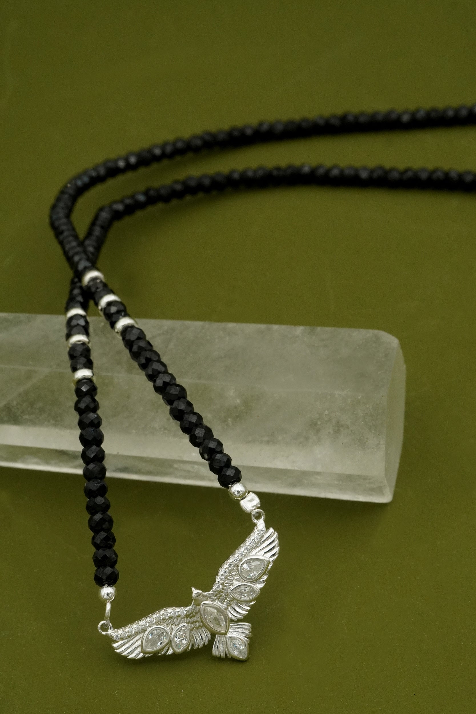 Black beaded necklace with a silver NZ hawk pendant on a green background