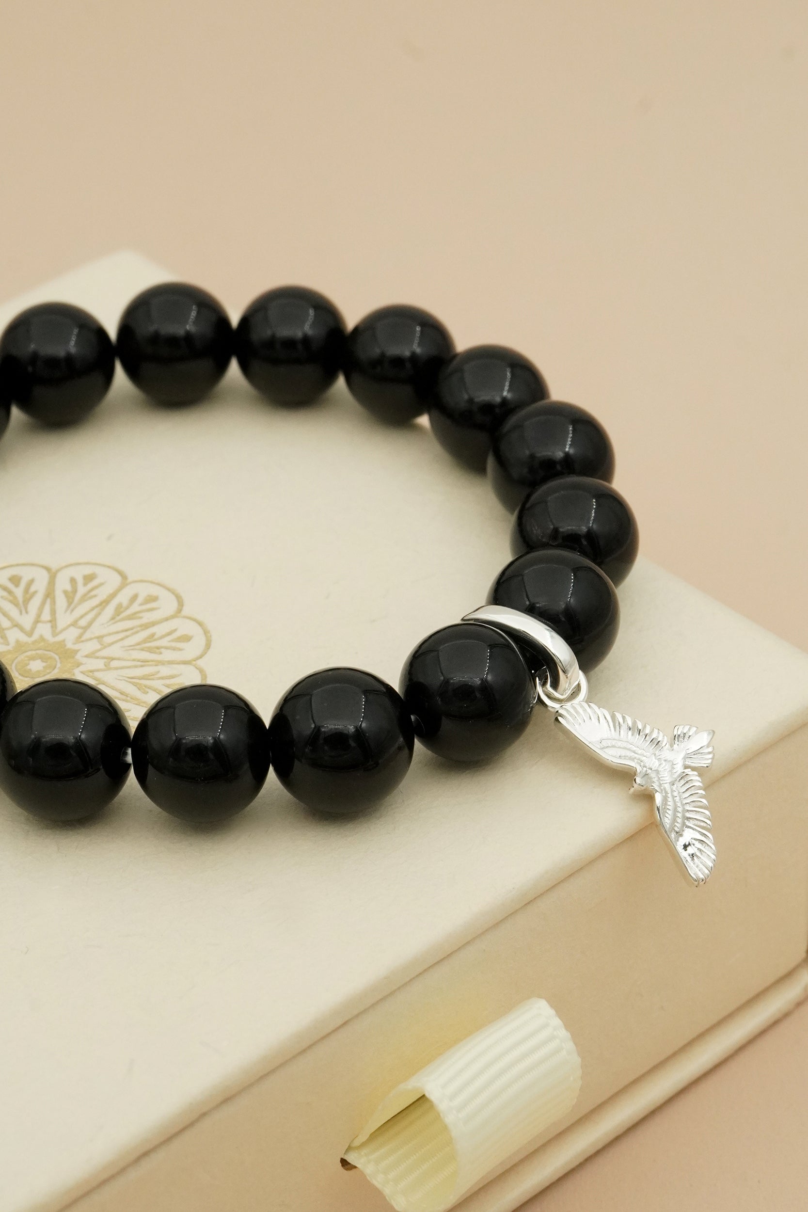 Black agate crystal beaded bracelet with a silver eagle charm on a beige surface
