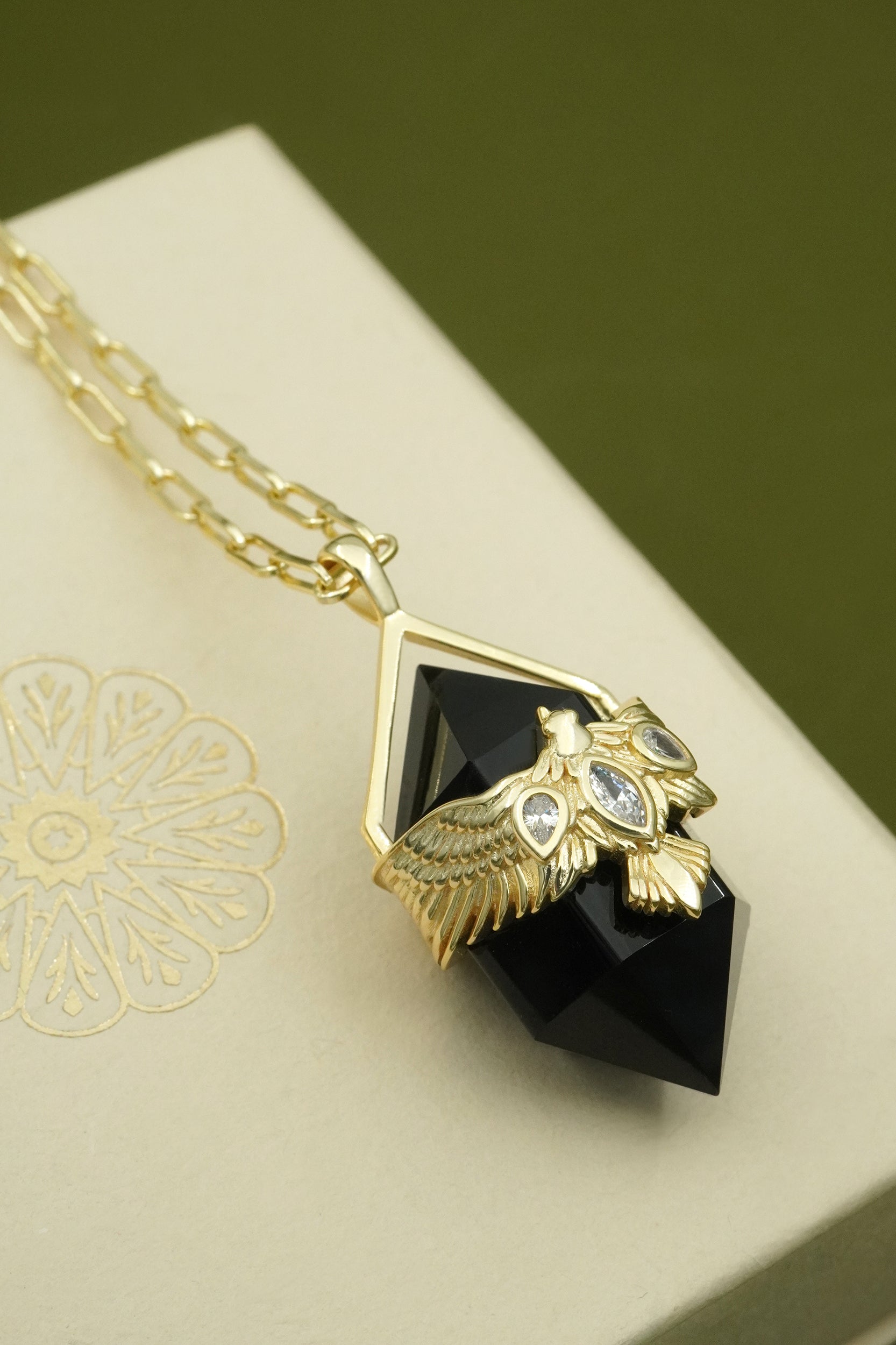 Gold necklace with a hawk bird pendant on a decorative box
