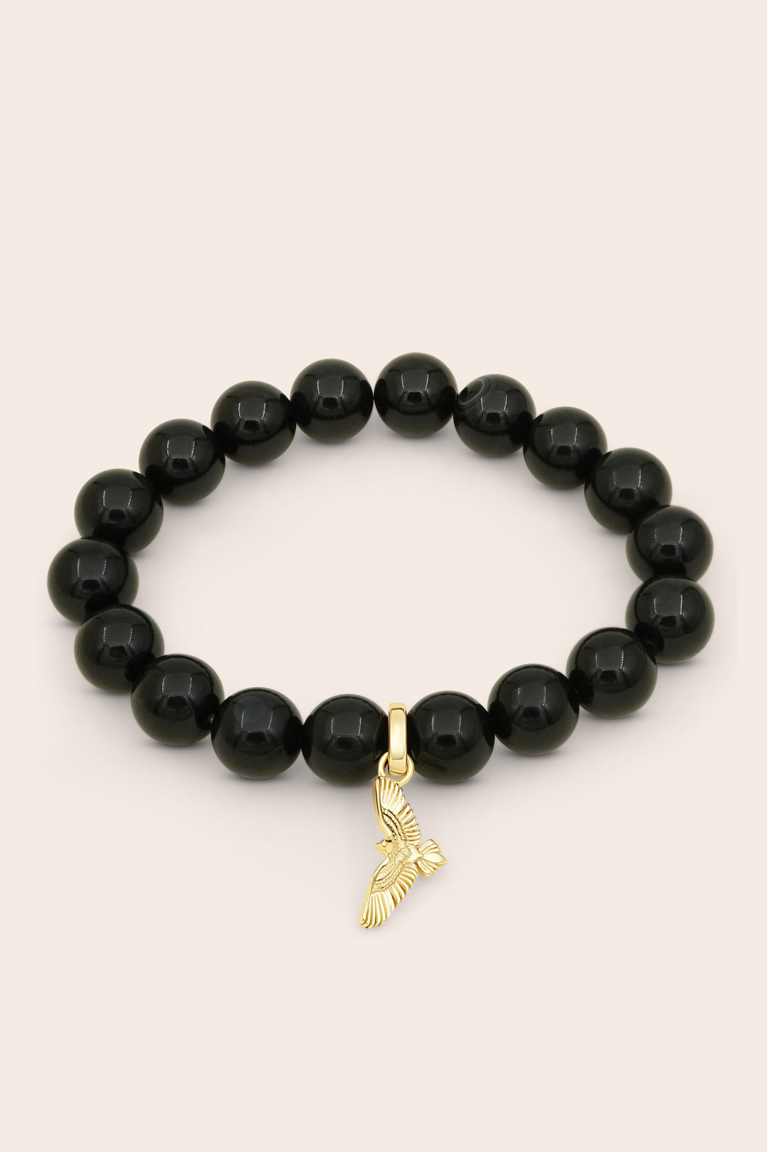 Black agate beaded bracelet with a gold soaring hawk bird charm on a beige background