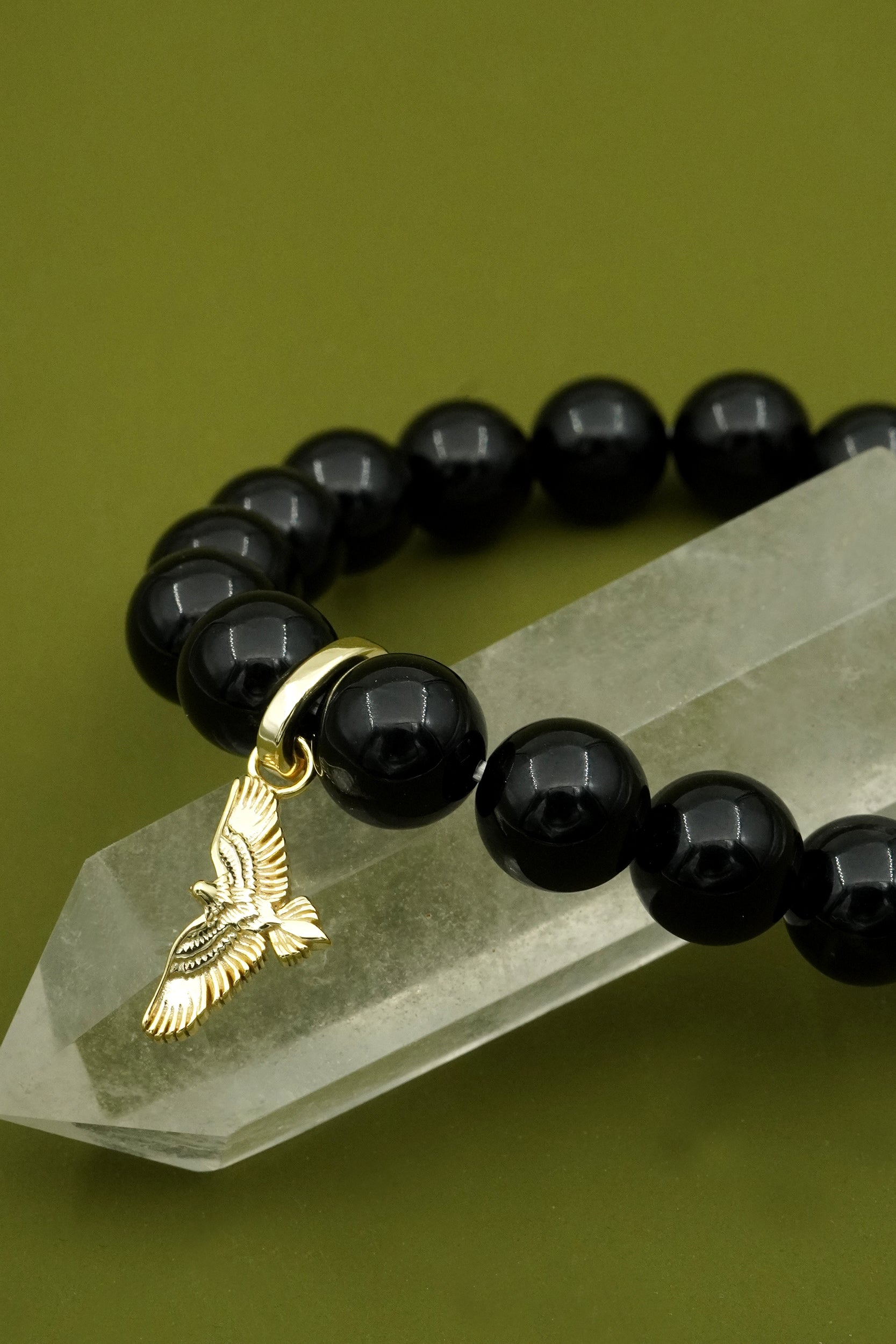 Black agate beaded bracelet with a gold eagle charm on a green stone against a green background for protection