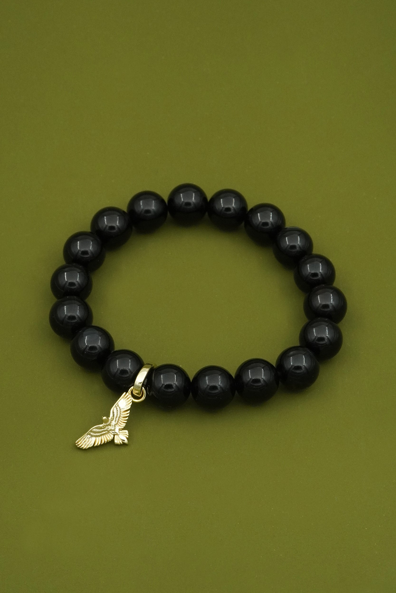 Black agate crystal beaded bracelet with a gold eagle wings charm on a green background