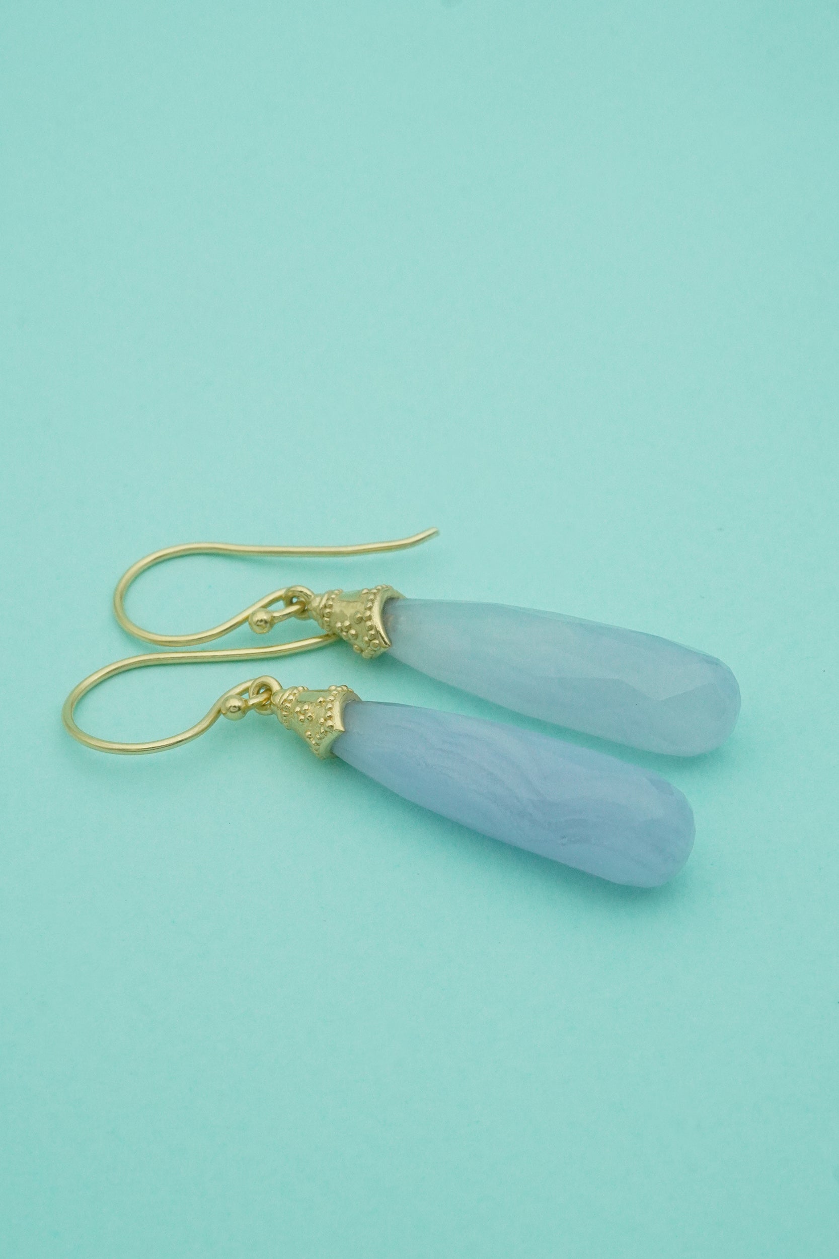Pair of light blue lace gate earrings with gold hooks on a teal background