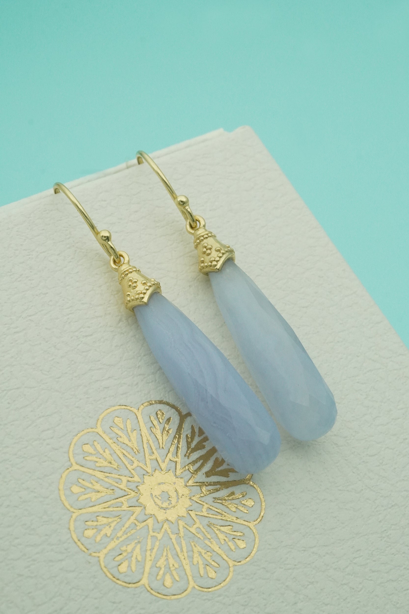 Blue crystal teardrop earrings with gold accents on a decorative card against a teal background