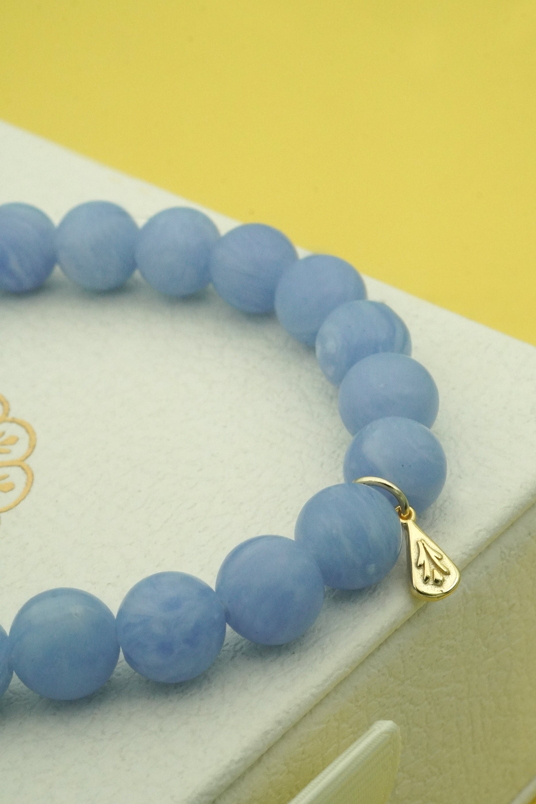 Blue beaded bracelet with a gold charm on a white surface with a yellow background