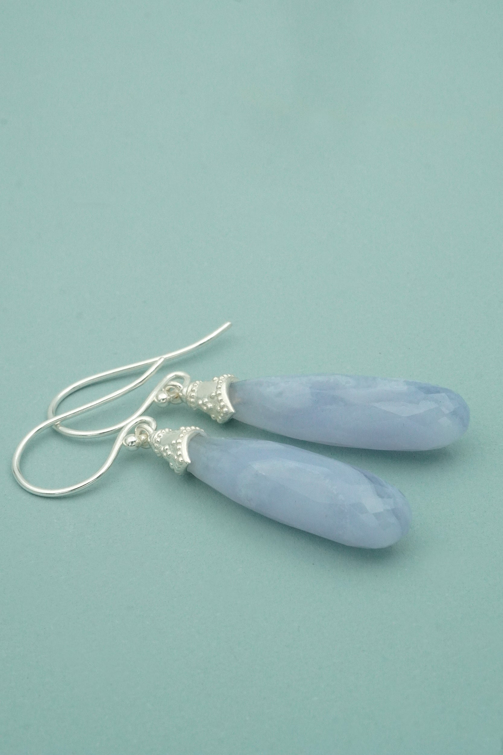 Pair of blue lace agate teardrop earrings on a light blue background