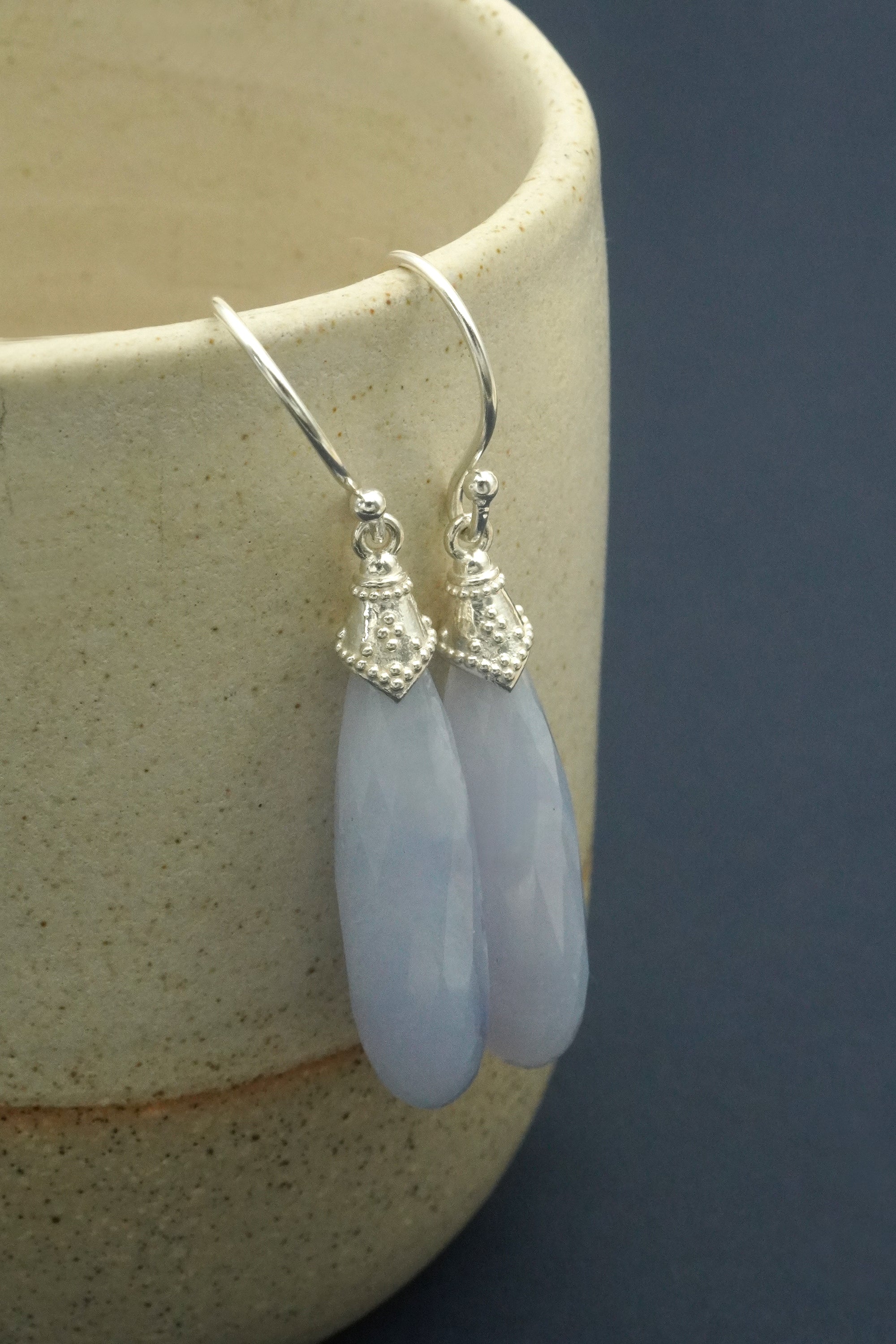 Blue lace agate crystal teardrop earrings with silver hooks on a ceramic surface