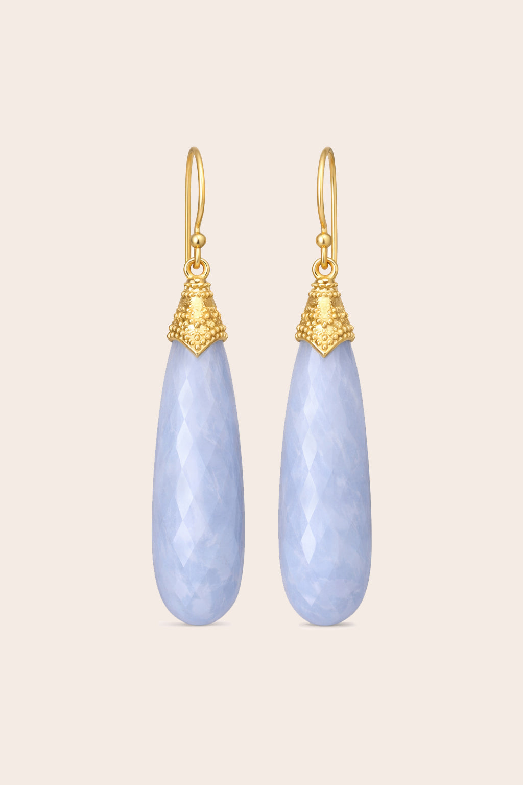 Pair of gold and blue lace teardrop earrings on a beige background