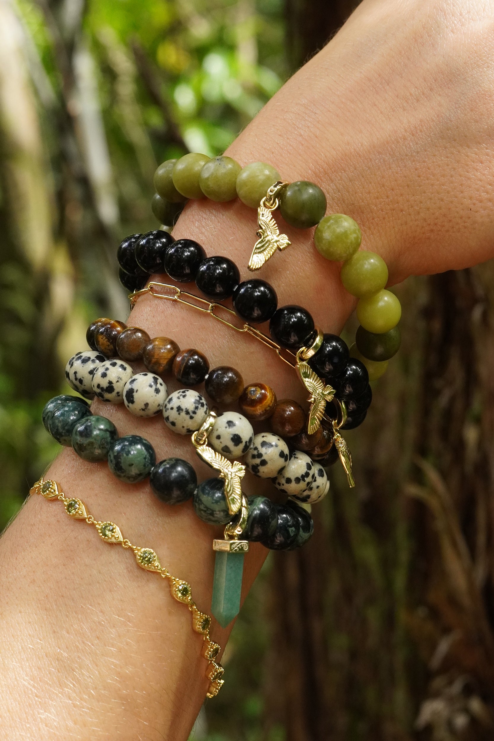 Stack of green and brown gemstone beaded bracelets on a wrist with a natural NZ first background